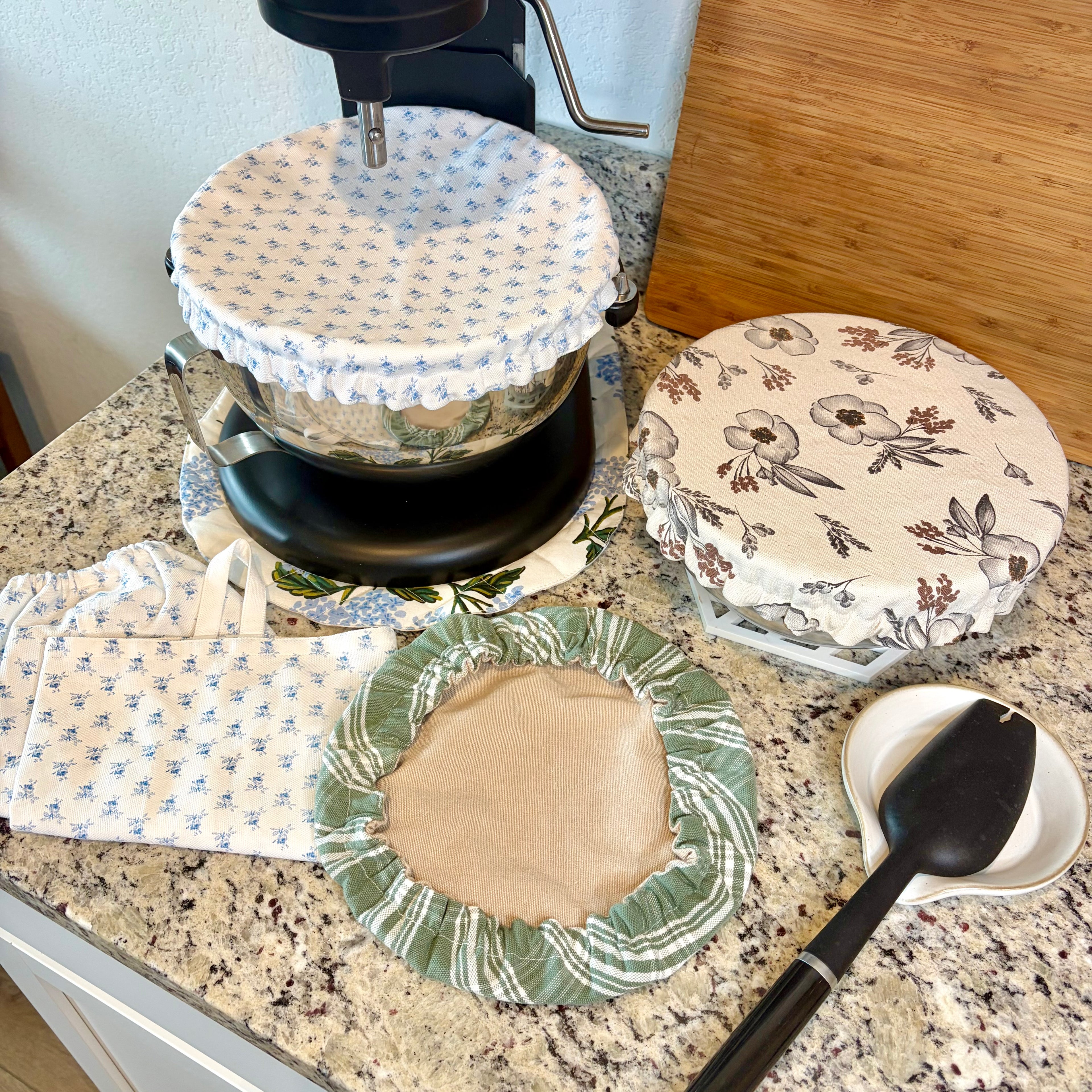 collection o 3 bowl covers, fabric spoon mixing tool and cutting board on a gray counter