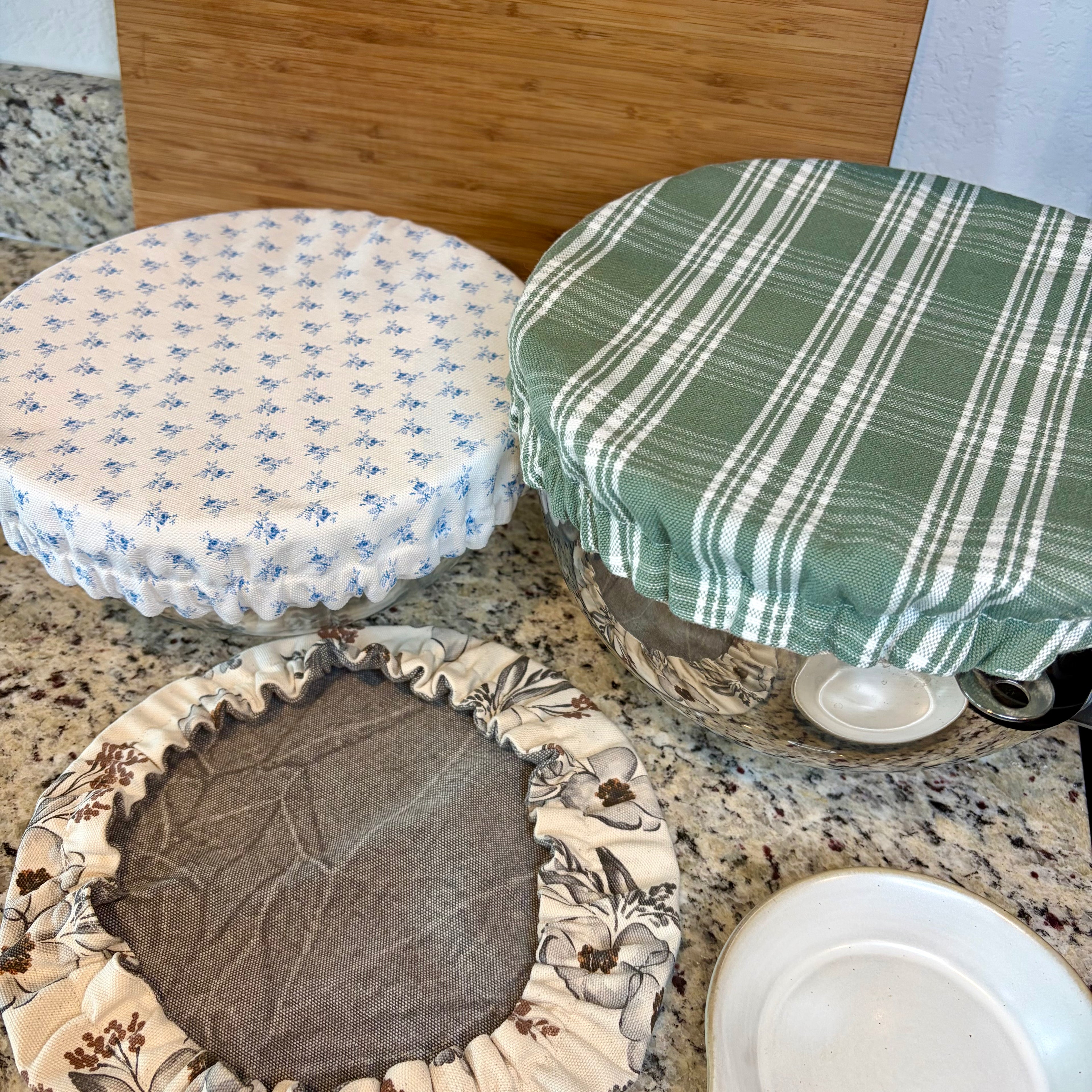 three bowl covers in white with blue, green and white plaid and gray/neutral floral on a gray counter
