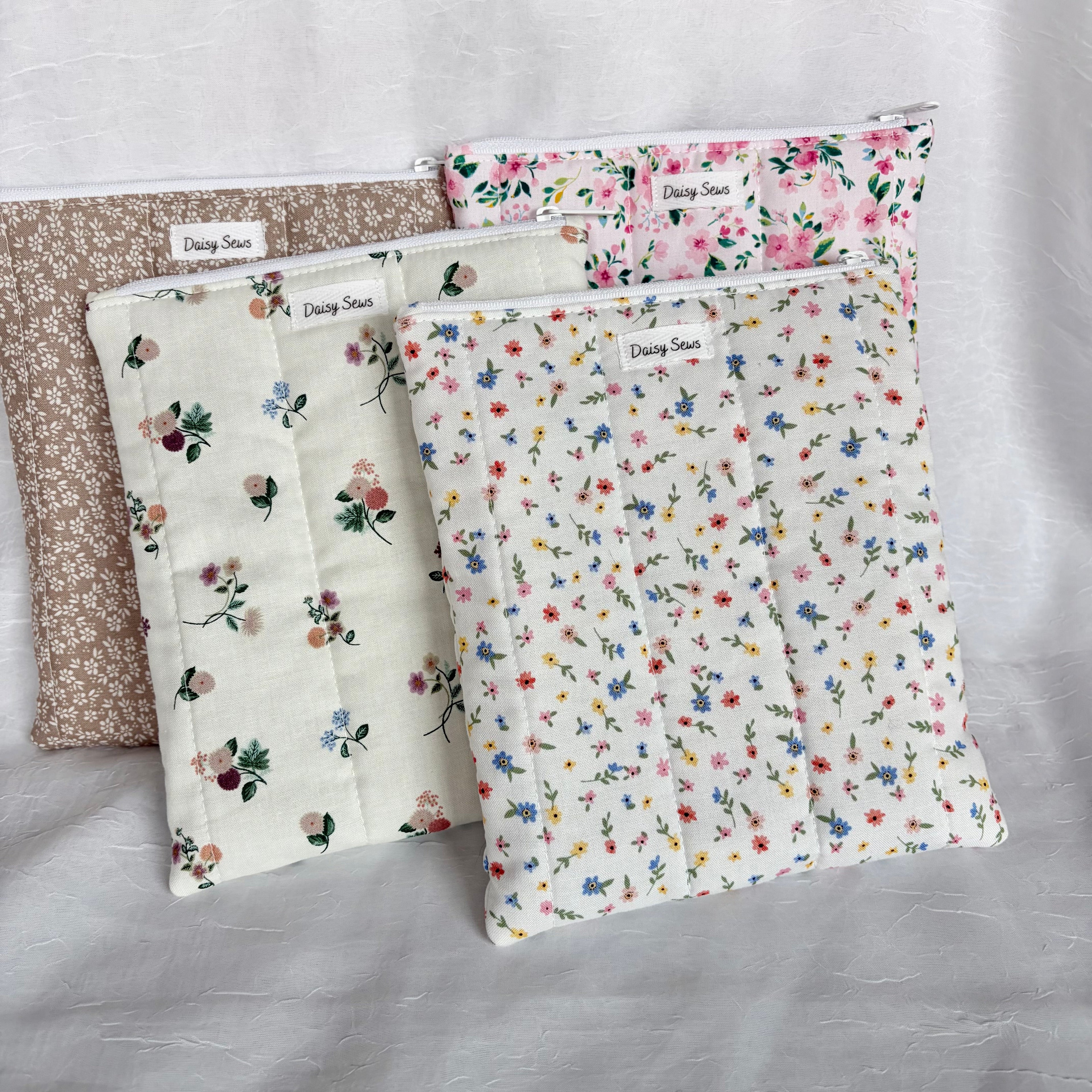 4 e-reader sleeves in brown, pink, neutral and colorful florals vertically stacked leaning on white backdrop