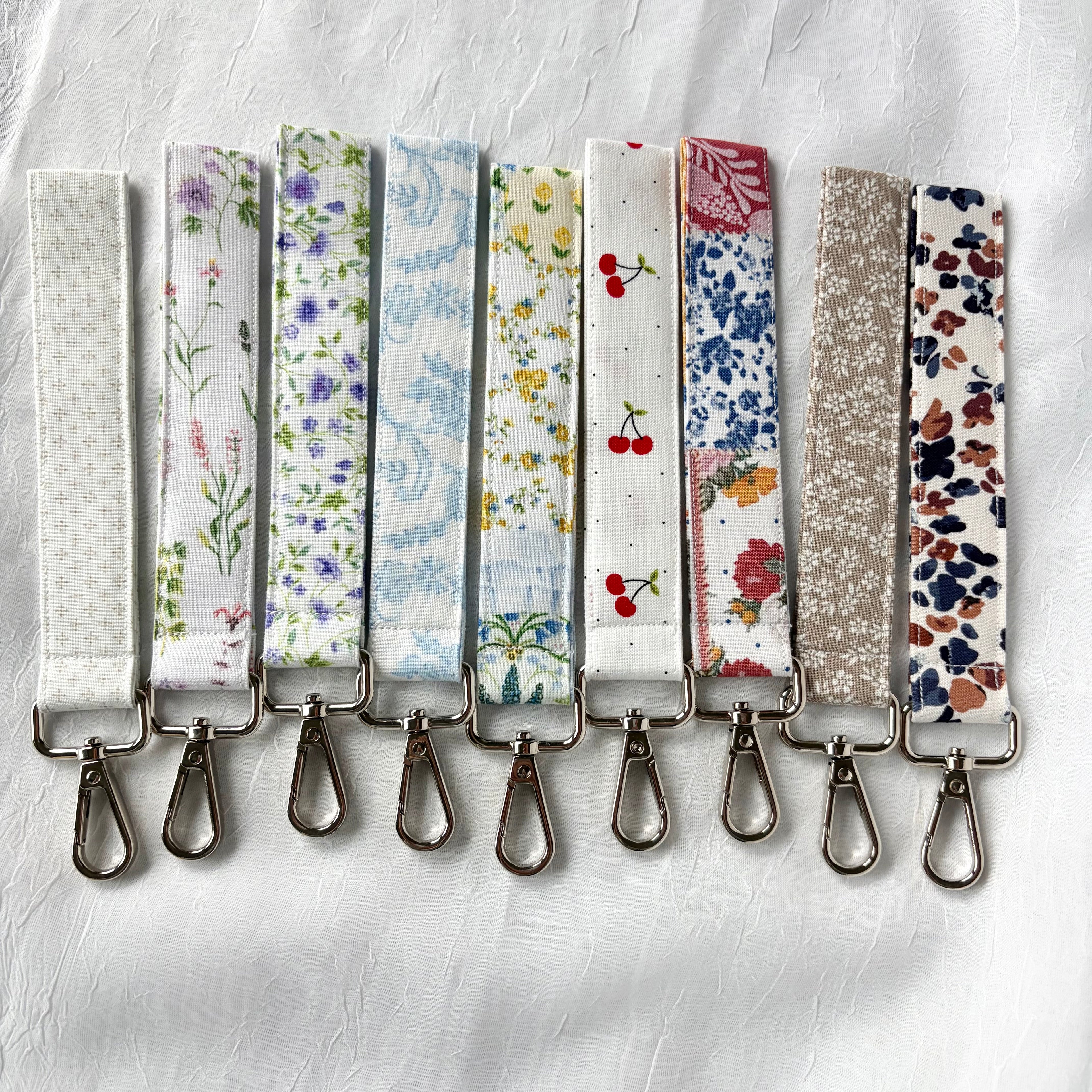 9 keychains in various colors and prints laying on a white surface with big silves clip