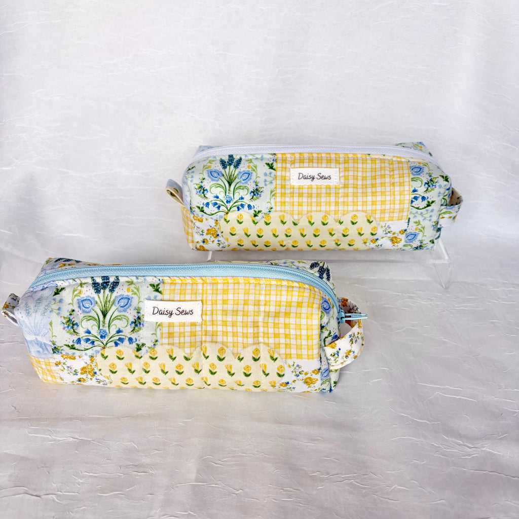 two blue and yellow floral patchwork boxy bags against white background. Front bag has light blue zipper and back bag has white zipper