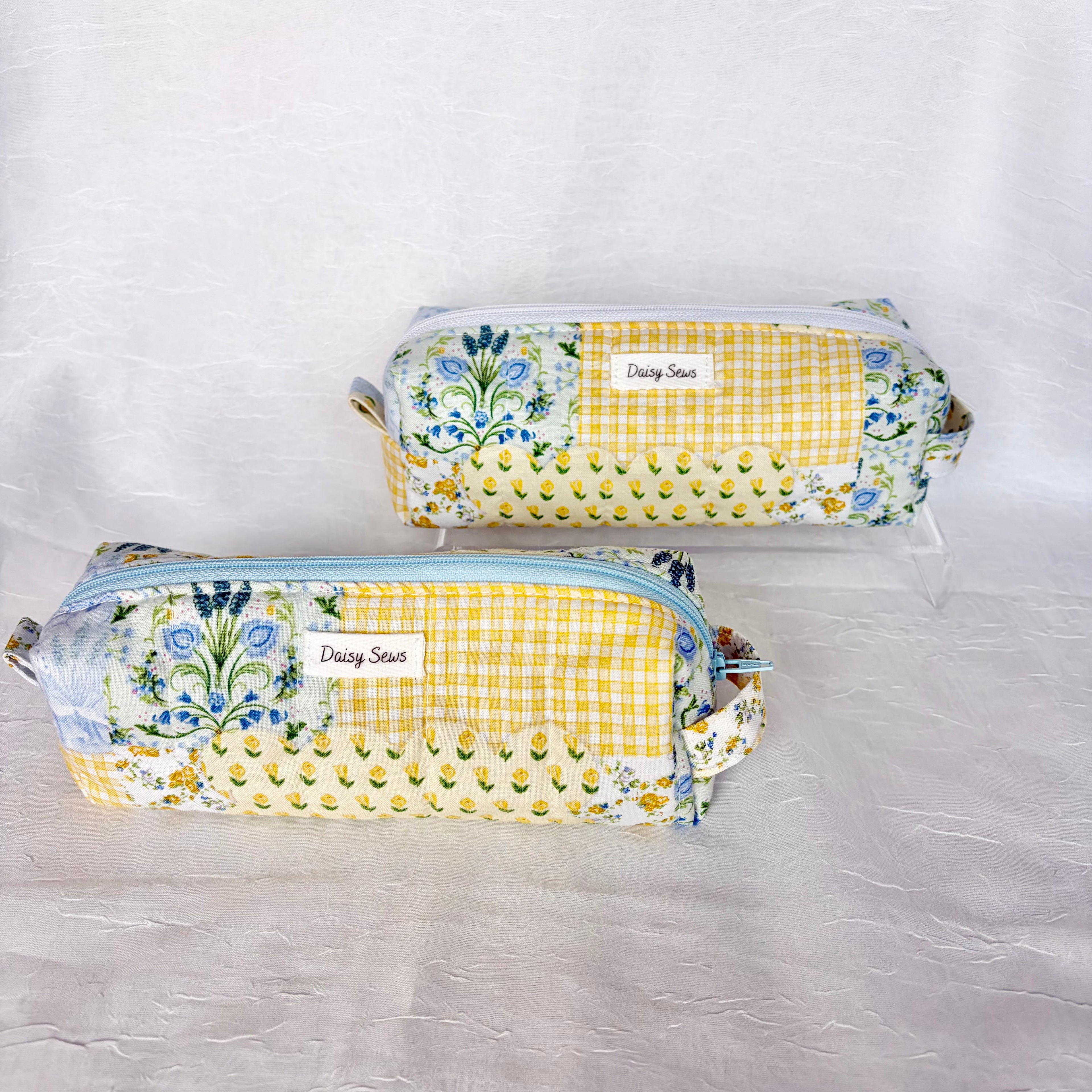 two blue and yellow floral patchwork boxy bags against white background. Front bag has light blue zipper and back bag has white zipper