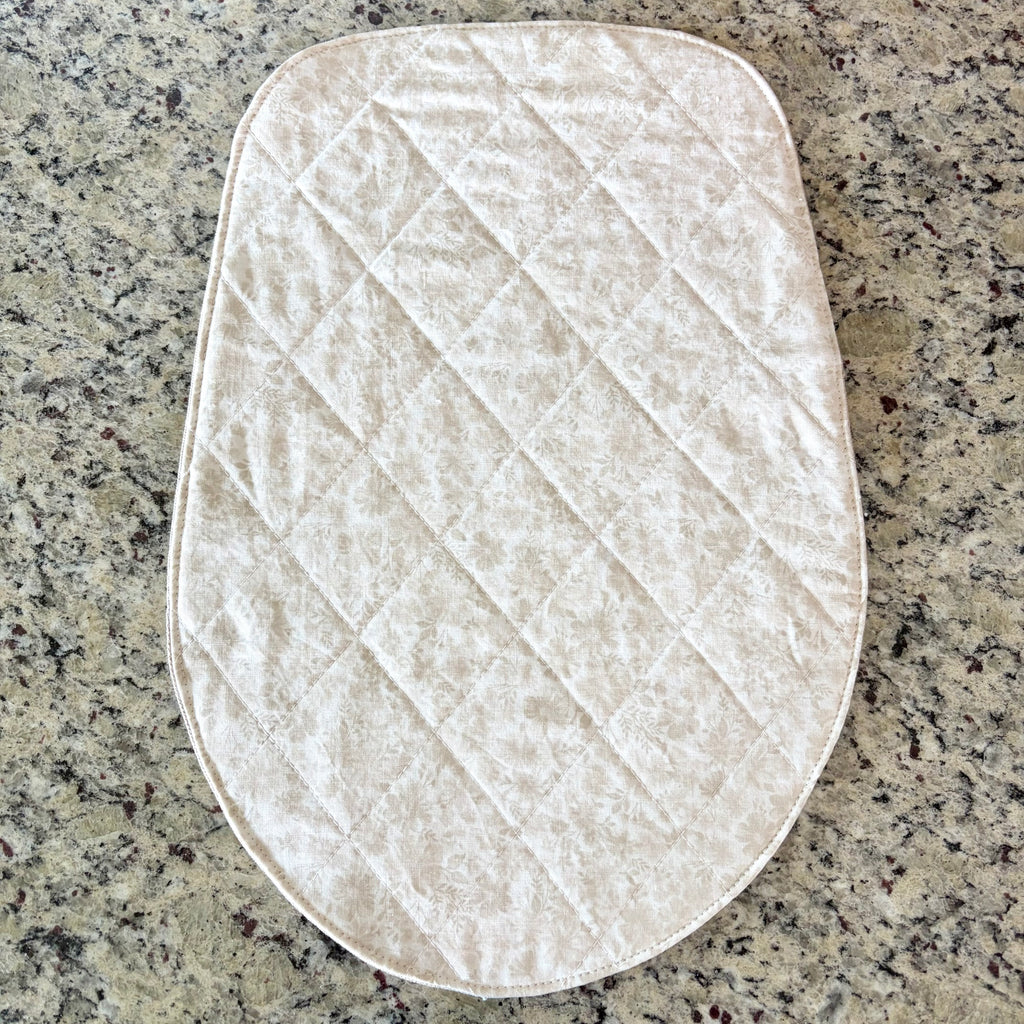 A quilted cream-colored floral fabric pad with a diamond pattern, laid flat on a speckled granite countertop. Head Tilt Size