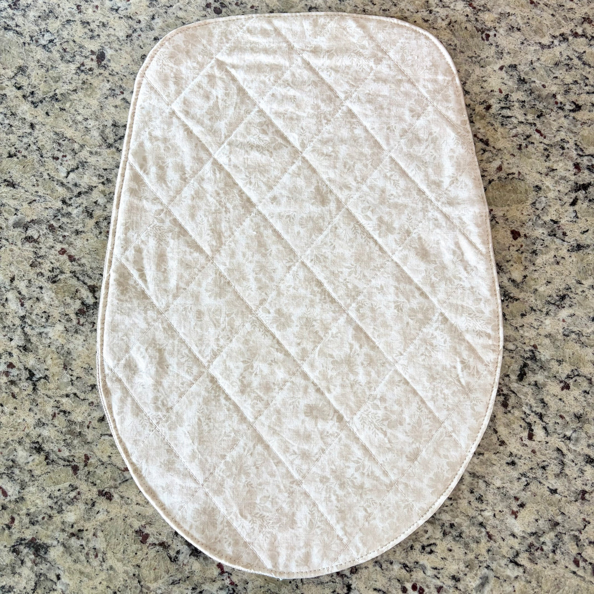 A quilted cream-colored floral fabric pad with a diamond pattern, laid flat on a speckled granite countertop. Head Tilt Size