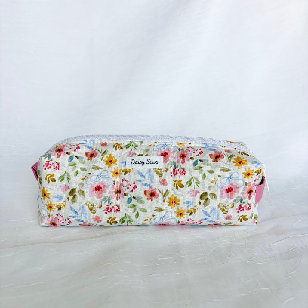 A fabric zippered pouch with a colorful floral print on a white background, featuring a small white label that reads 'Daily Sews'.