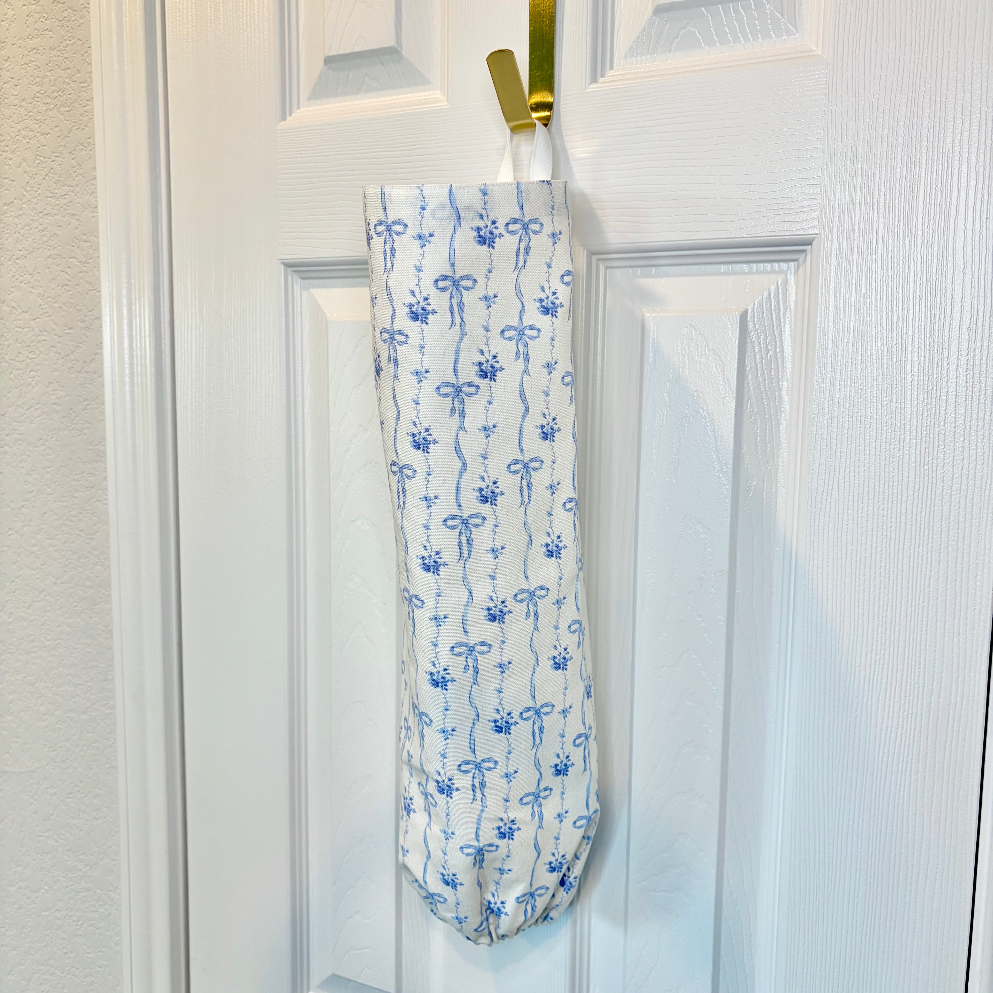 white Fabric Cylinder with bows in vertical pattern hanging on gold hook against white door