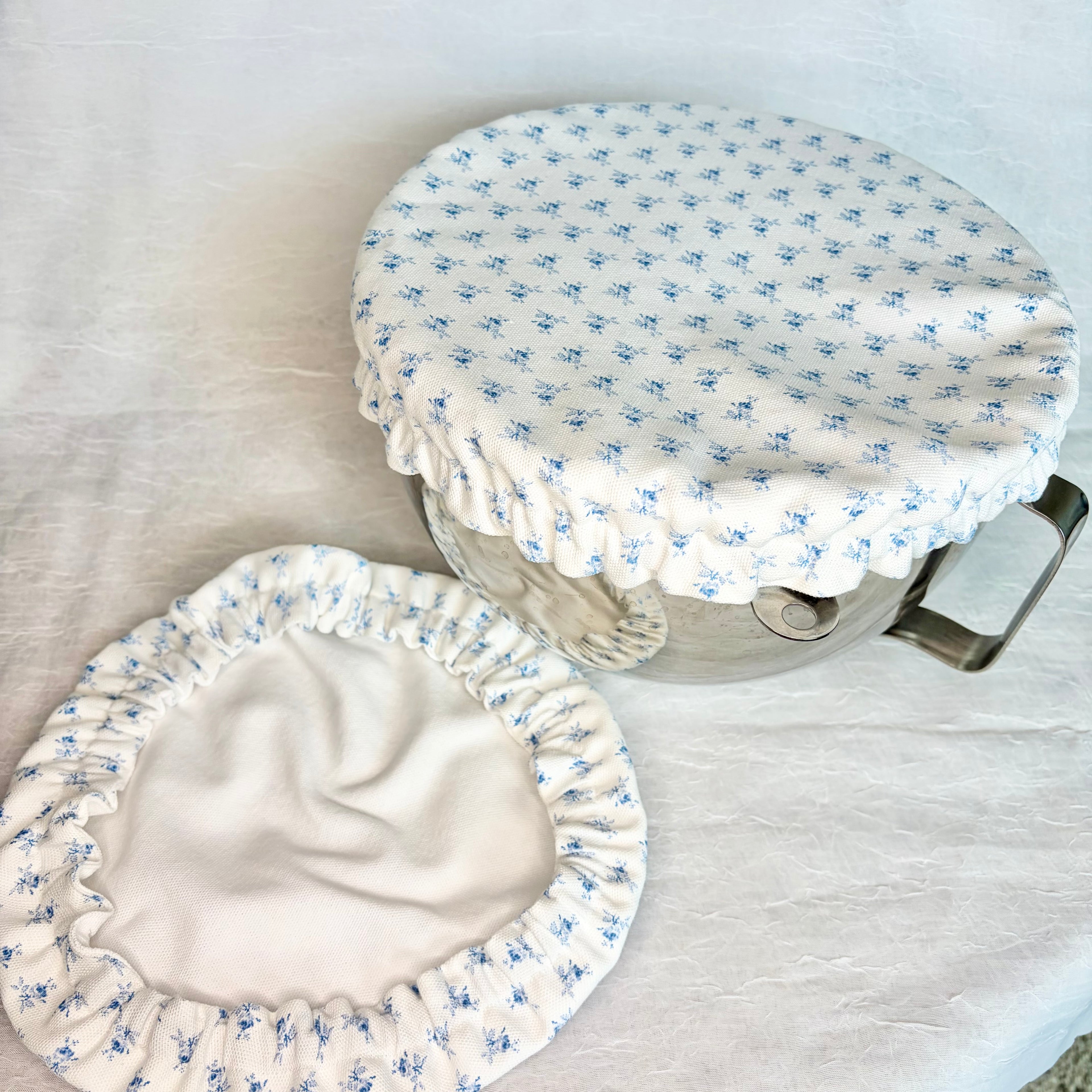 white with small blue flowers bowl cover on metal bowl with handle and same bowl cover on surface showing white on the second side