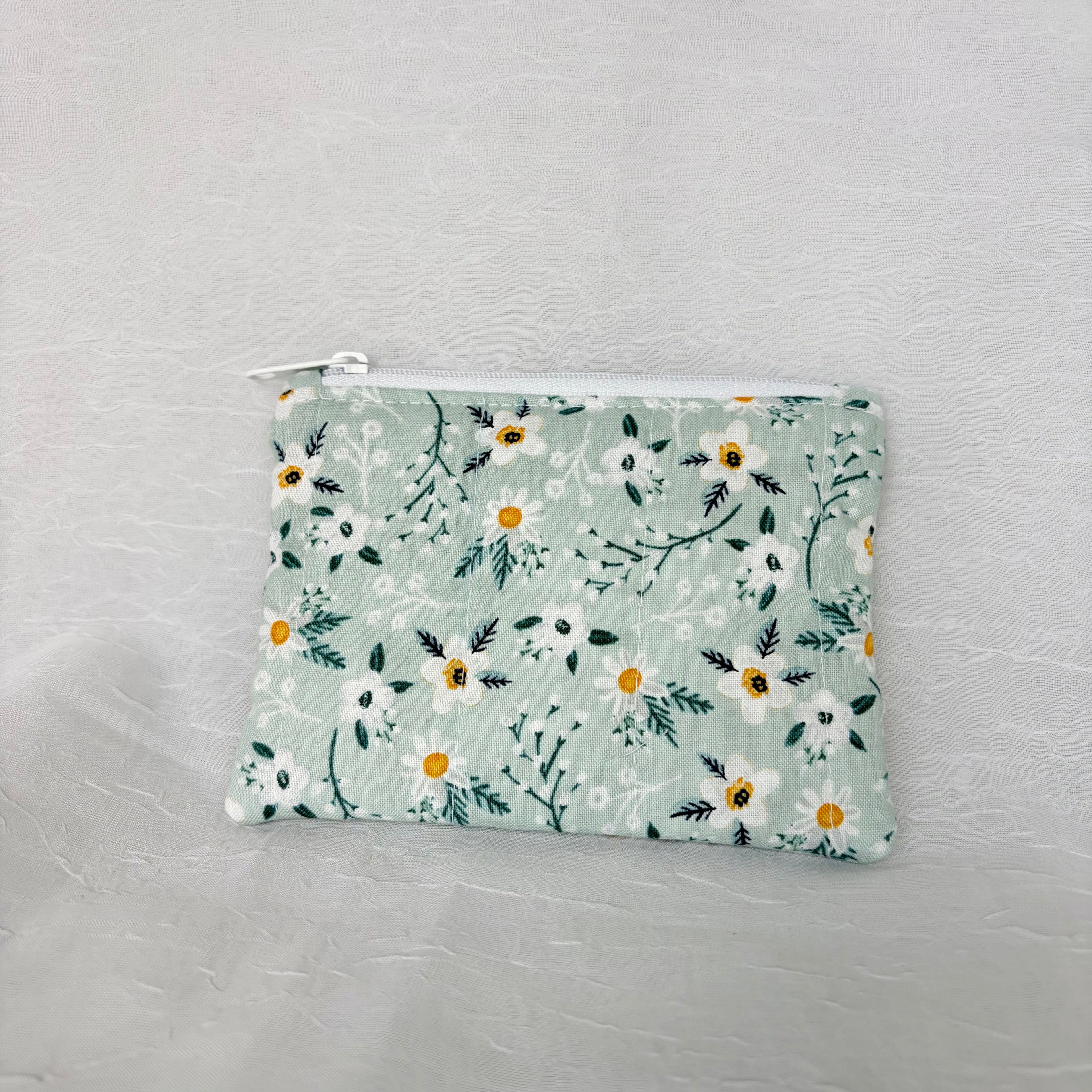 Back of Blue fabric with whit flowers and teal leaf patterned small pouch with white zipper on white background