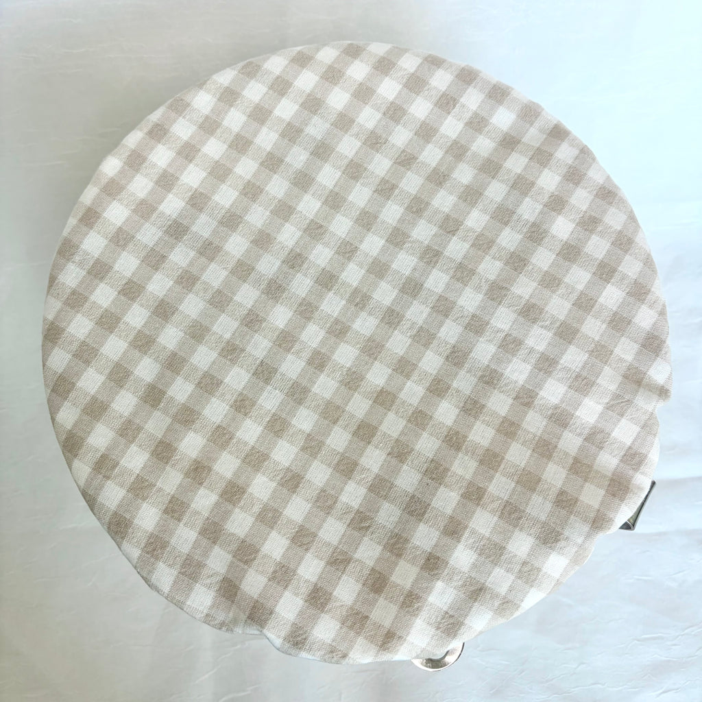A round fabric-covered bowl , featuring a beige and white gingham checkered pattern, photographed from directly above on a white background.
