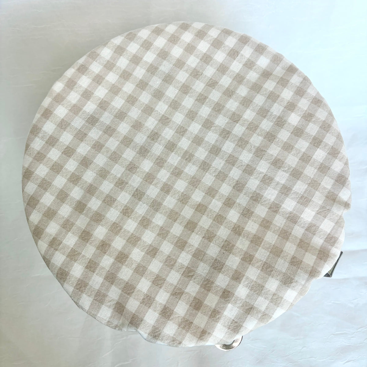A round fabric-covered bowl , featuring a beige and white gingham checkered pattern, photographed from directly above on a white background.