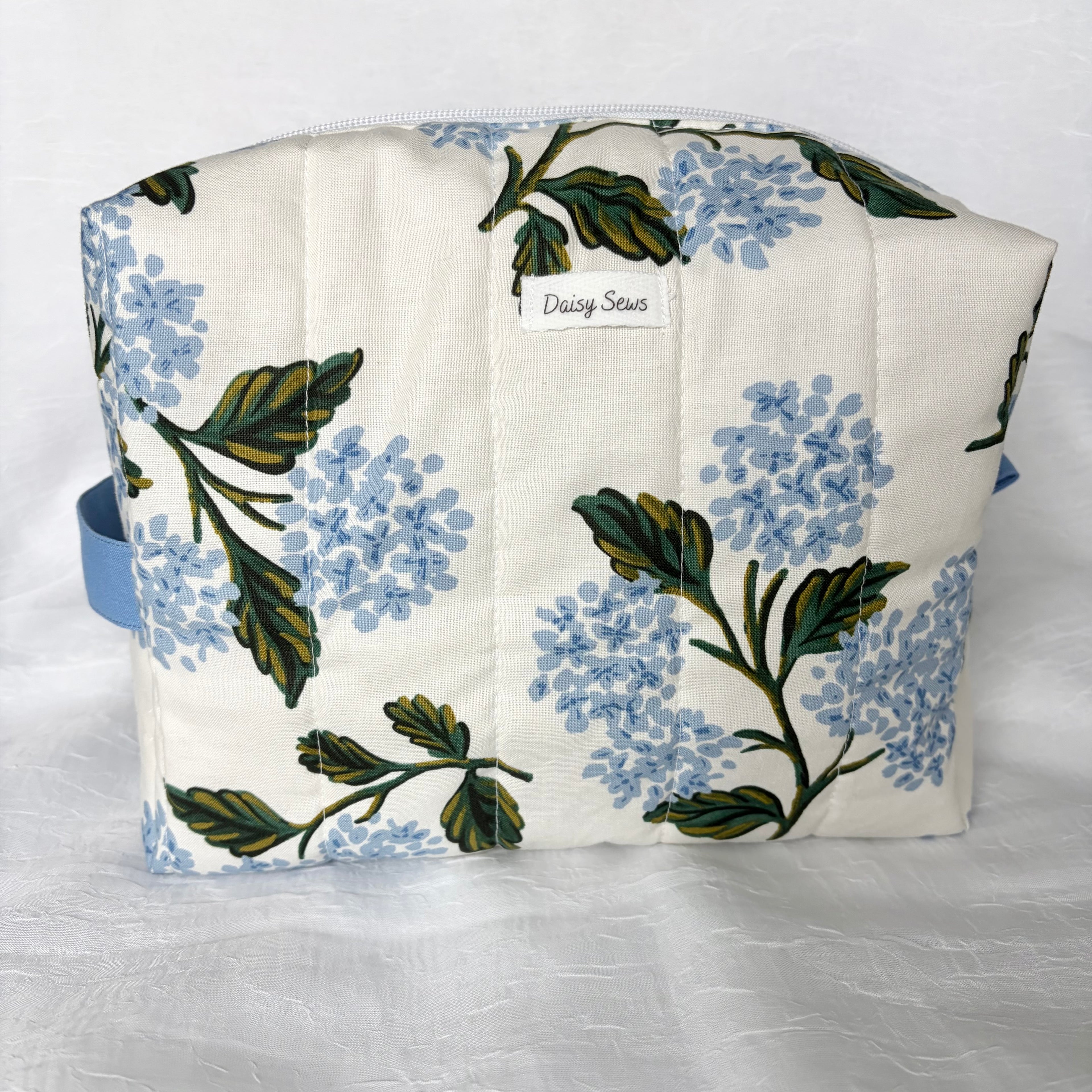 large blue hydrangea and green leaf designed boxy bag with white label and blue accents on white background