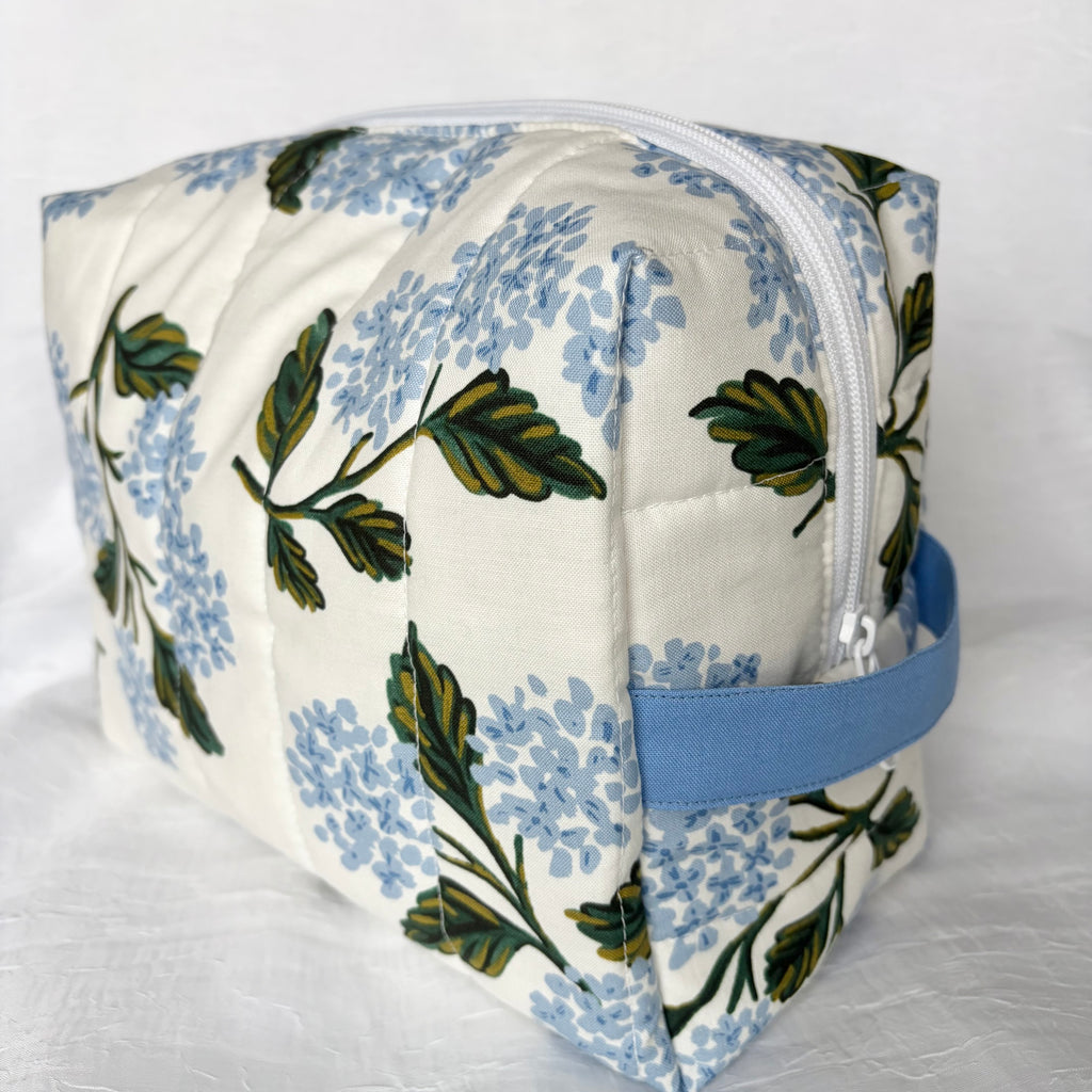 Side view of blue handle and white zipper on large blue hydrangea and green leaf designed boxy bag on white background