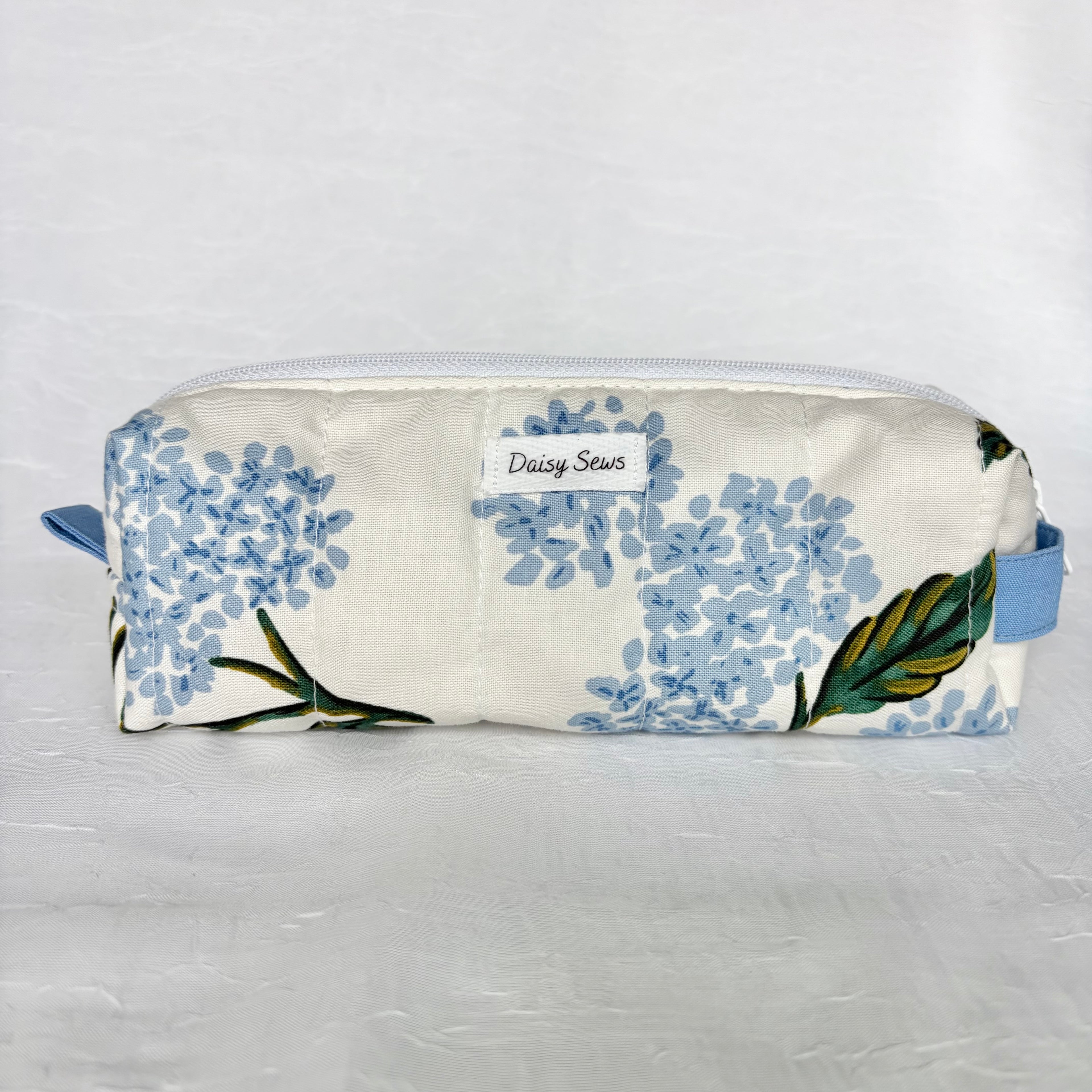 Blue Hydrangea-patterned pouch with 'Daisy Sews' branding on a light gray background. Matching blue handle and pulltab