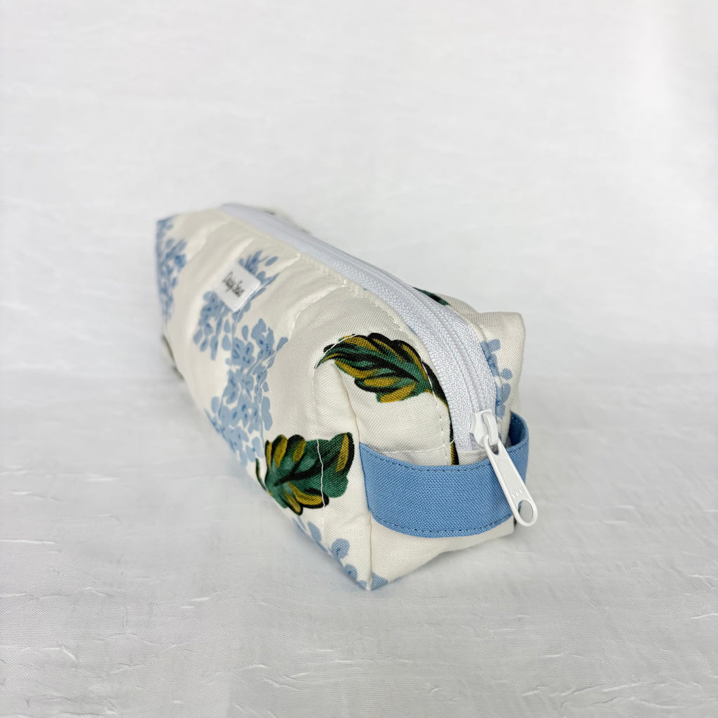 Blue Hydrangea-patterned pouch with green leaves, side view of blue handle on white background. 