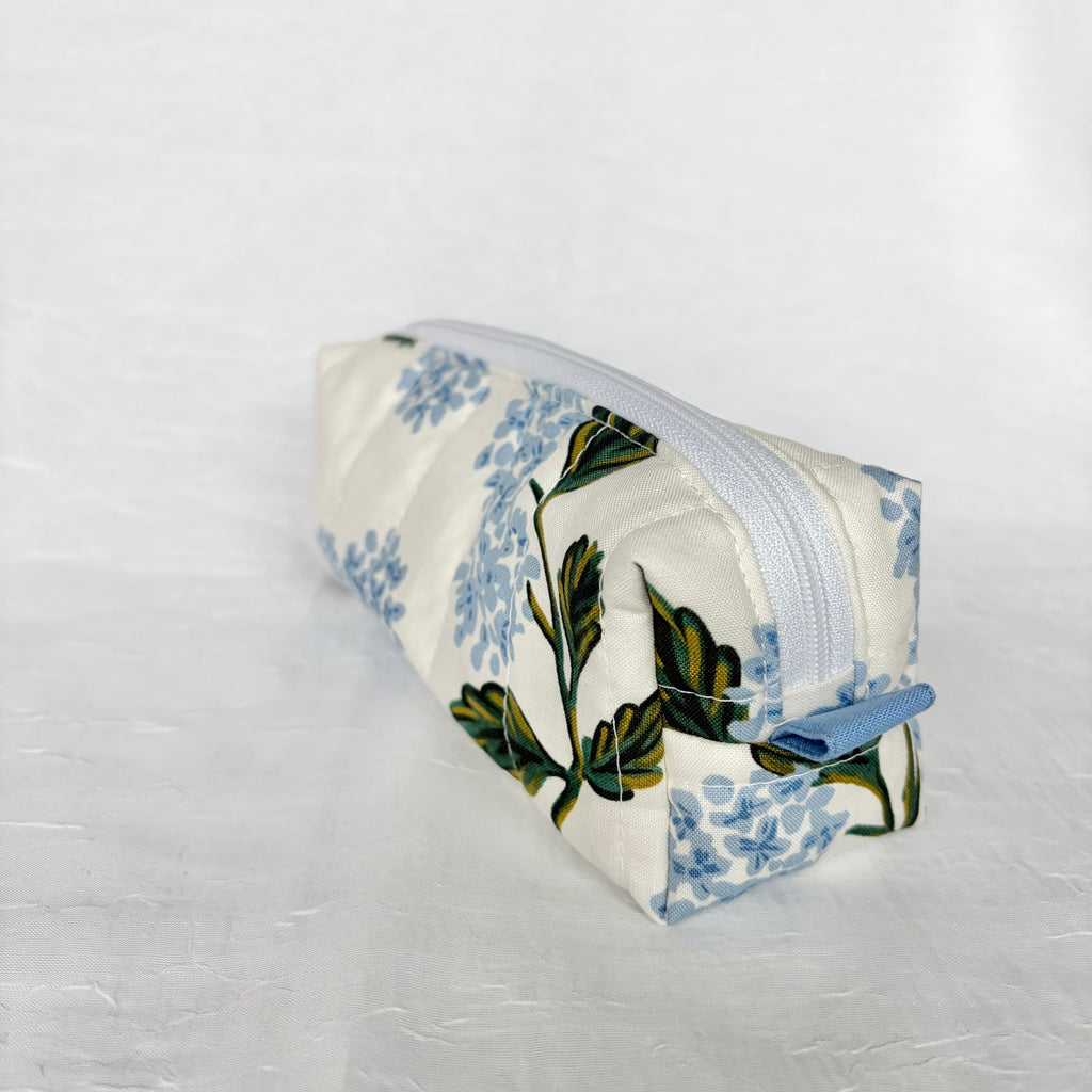 Blue Hydrangea-patterned pouch with green leaves side view of blue pull tab on white background. 