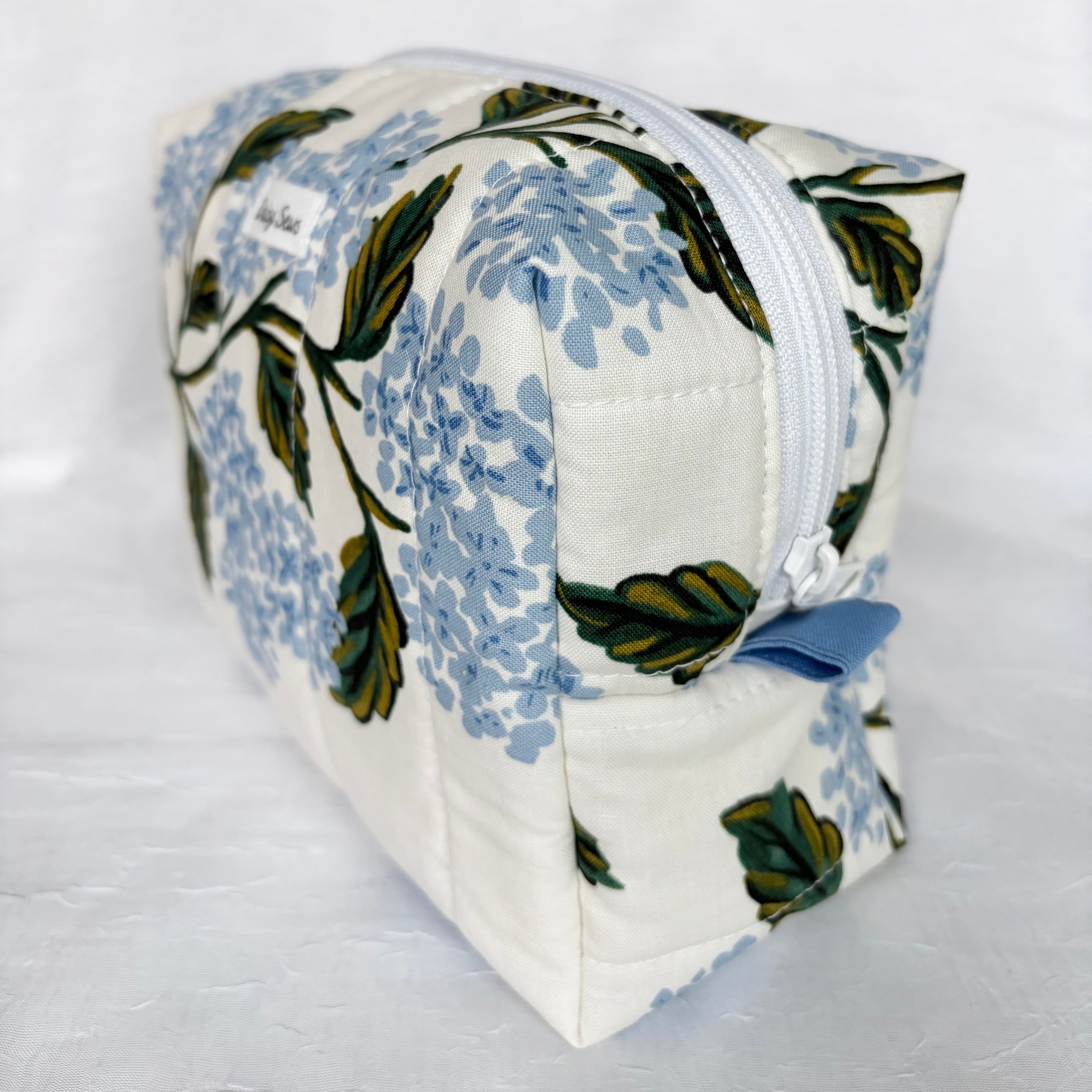 side view of blue pull tab and white zipper on large Blue Hydrangeas with green leaf design boxy bag on white background