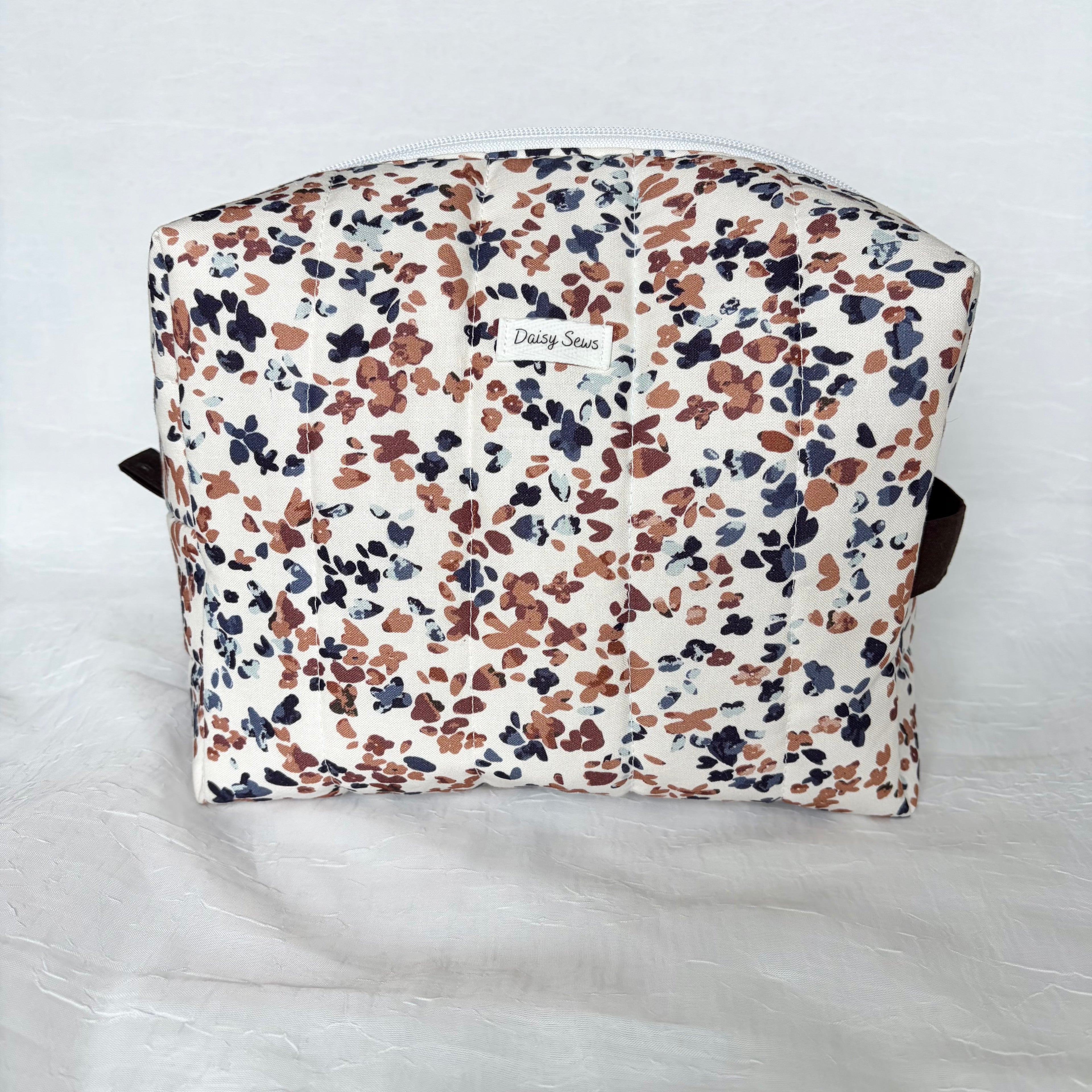 blue and mauve speckles on white large toiletry bag with white zipper and dark brown pull tab and handle with white logo on white background