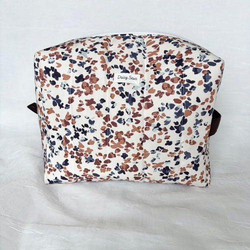 blue and mauve speckles on white large toiletry bag with white zipper and dark brown pull tab and handle with white logo on white background