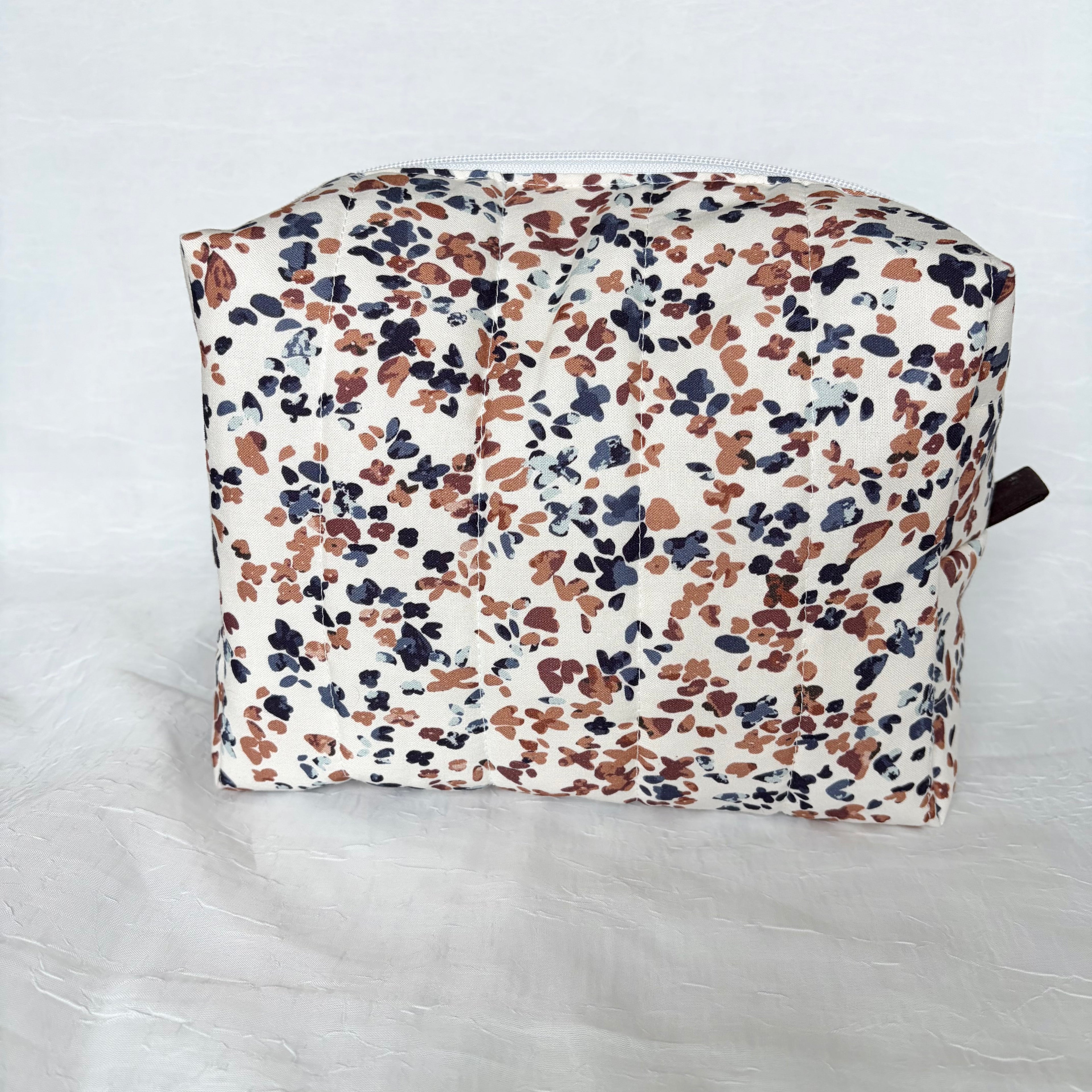 Back view of blue and mauve speckles on white large toiletry bag with white zipper and dark brown pull tab on white background