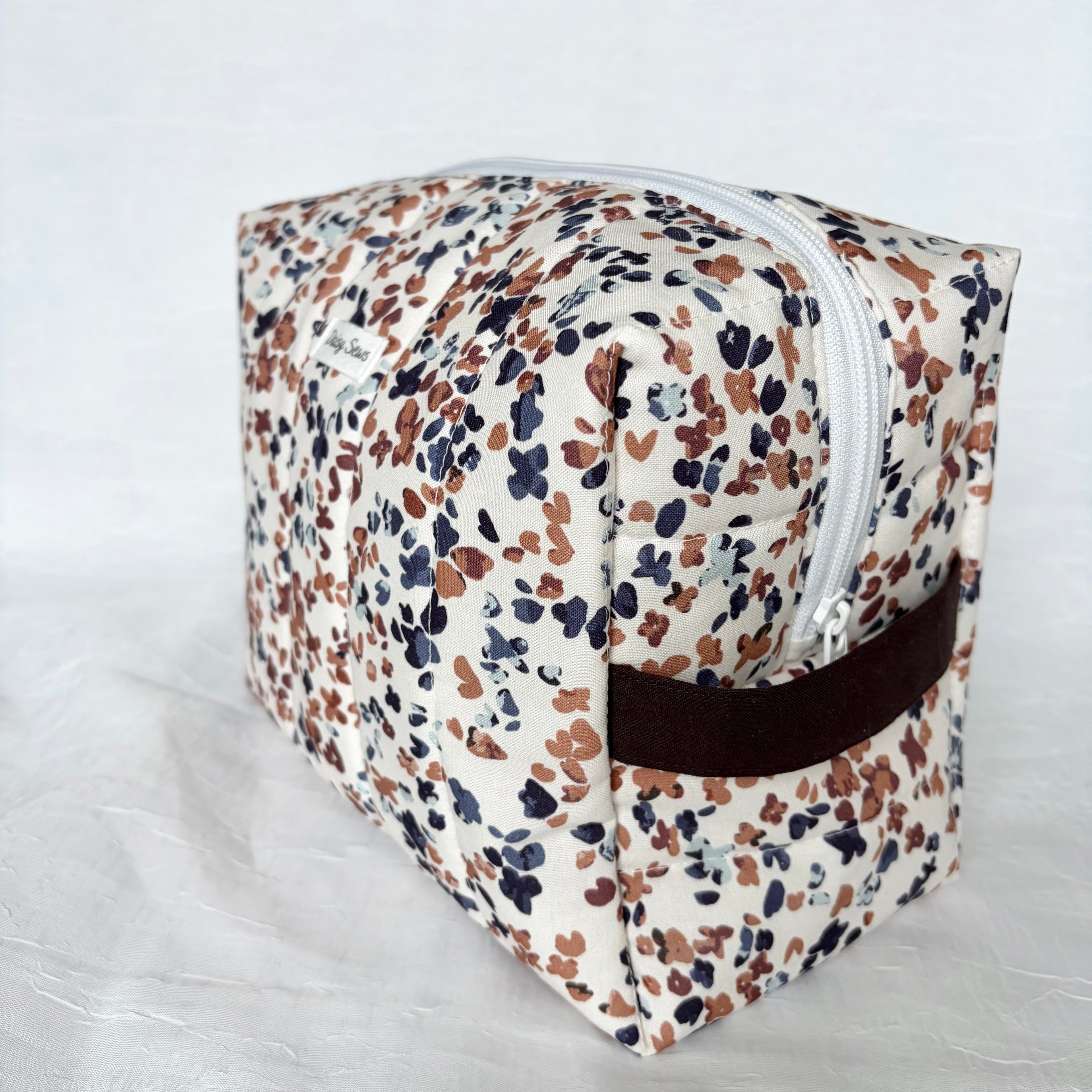 side view of dark brown handle and white zipper on blue and mauve speckles on white large toiletry bag on white background