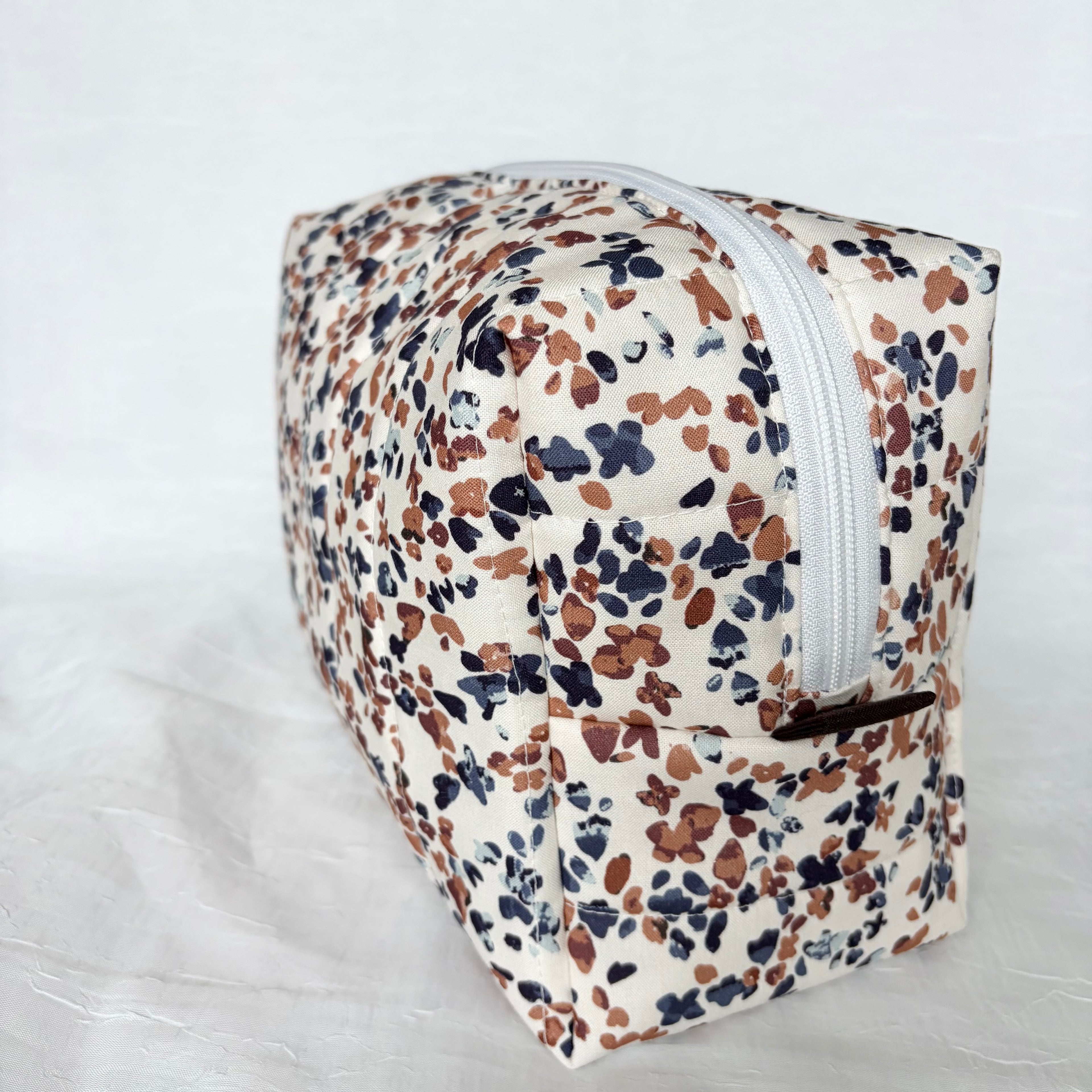side view of blue and mauve speckles on white large toiletry bag with white zipper and dark brown pull tab on white background
