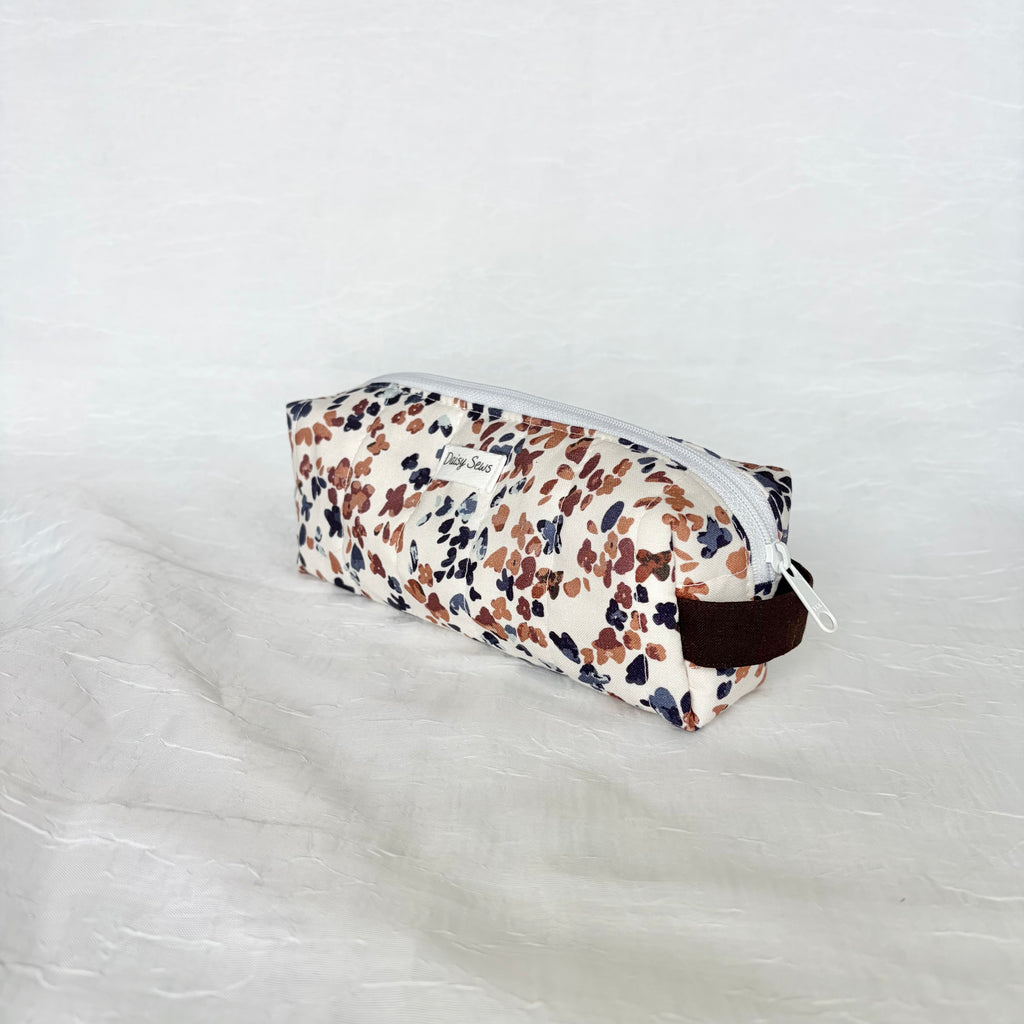 side view of dark brown handle and white zipper on a blue and mauve speckled white short and long bag on a white background with white label
