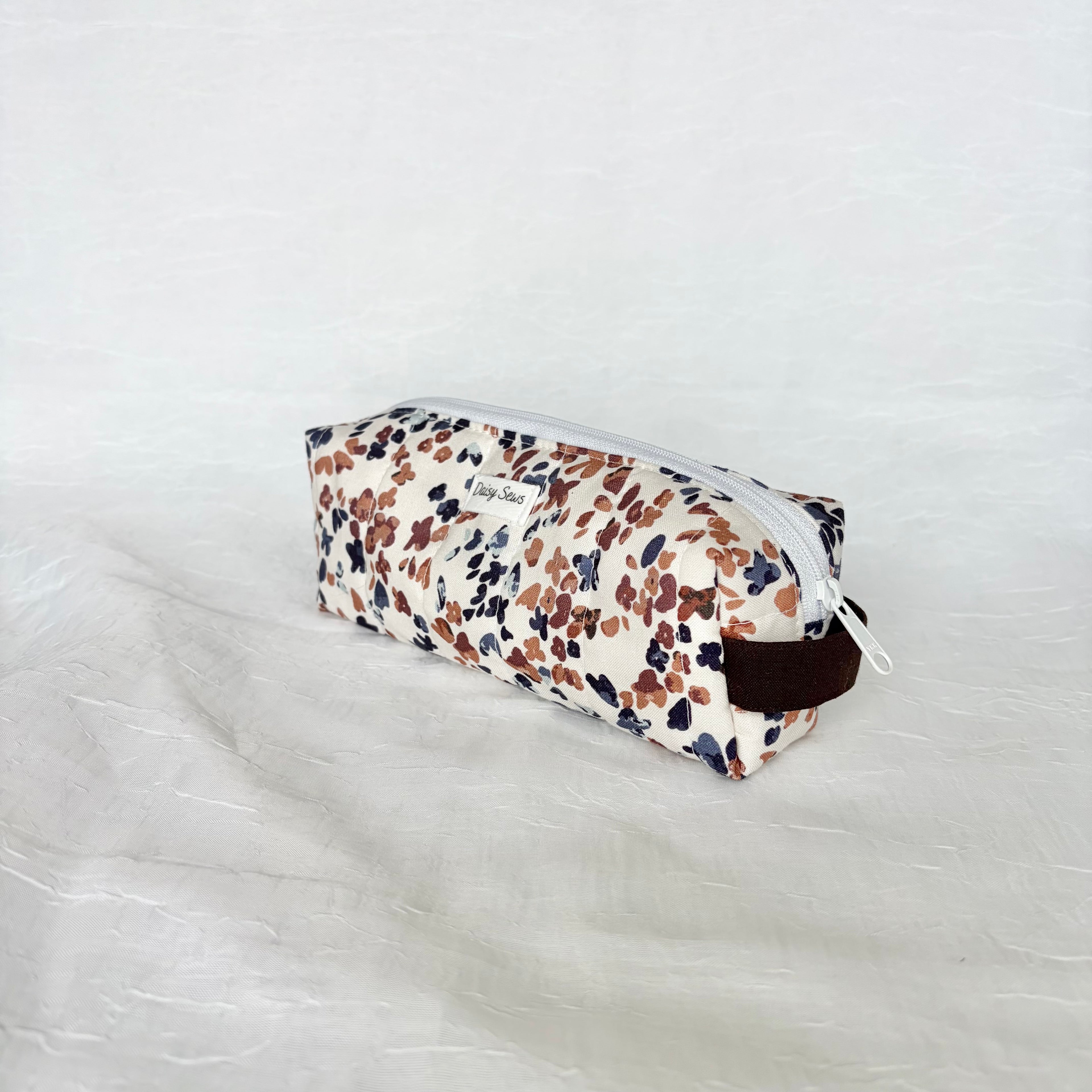 side view of dark brown handle and white zipper on a blue and mauve speckled white short and long bag on a white background with white label