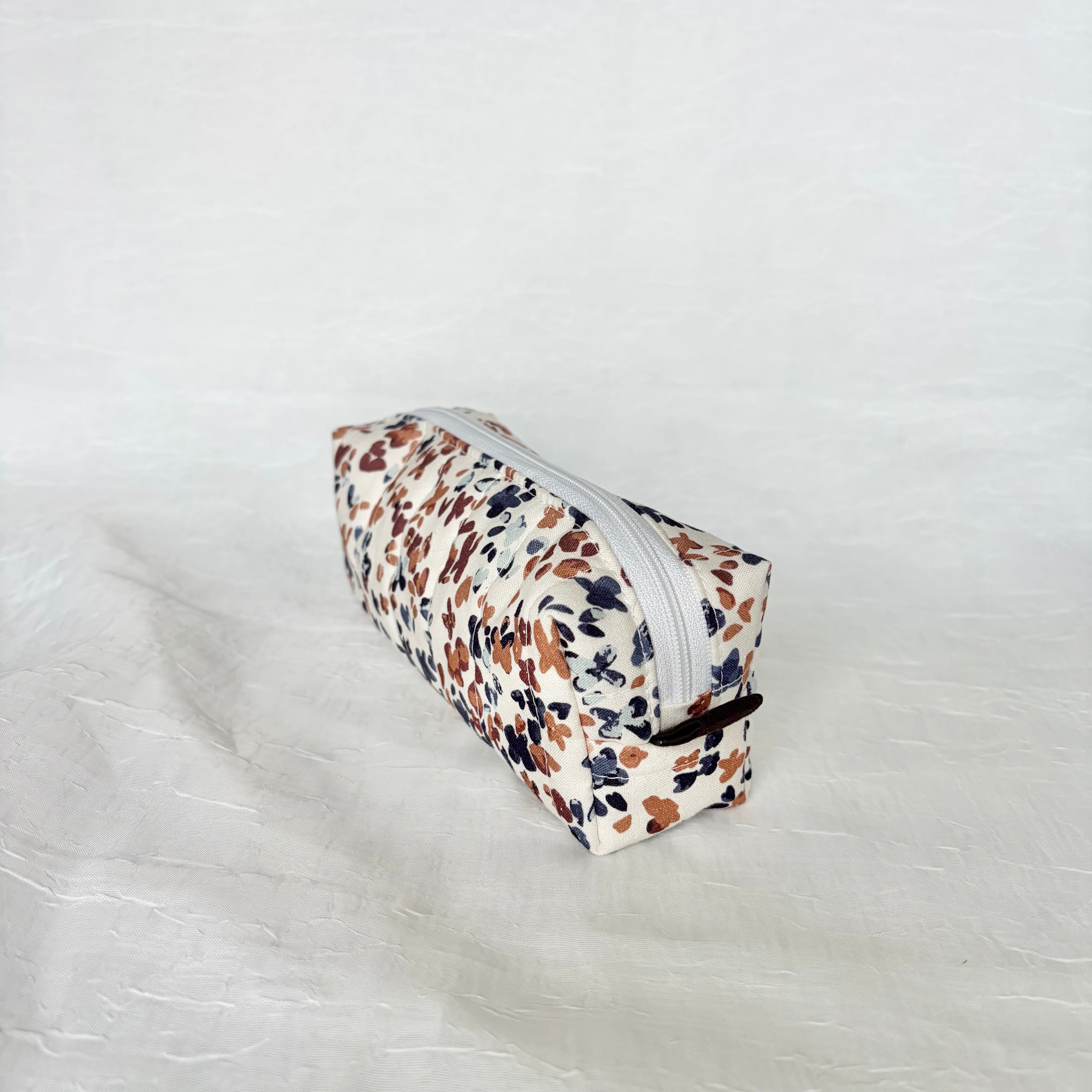 side view of dark brown tab and white zipper on a blue and mauve speckled white short and long bag on a white background