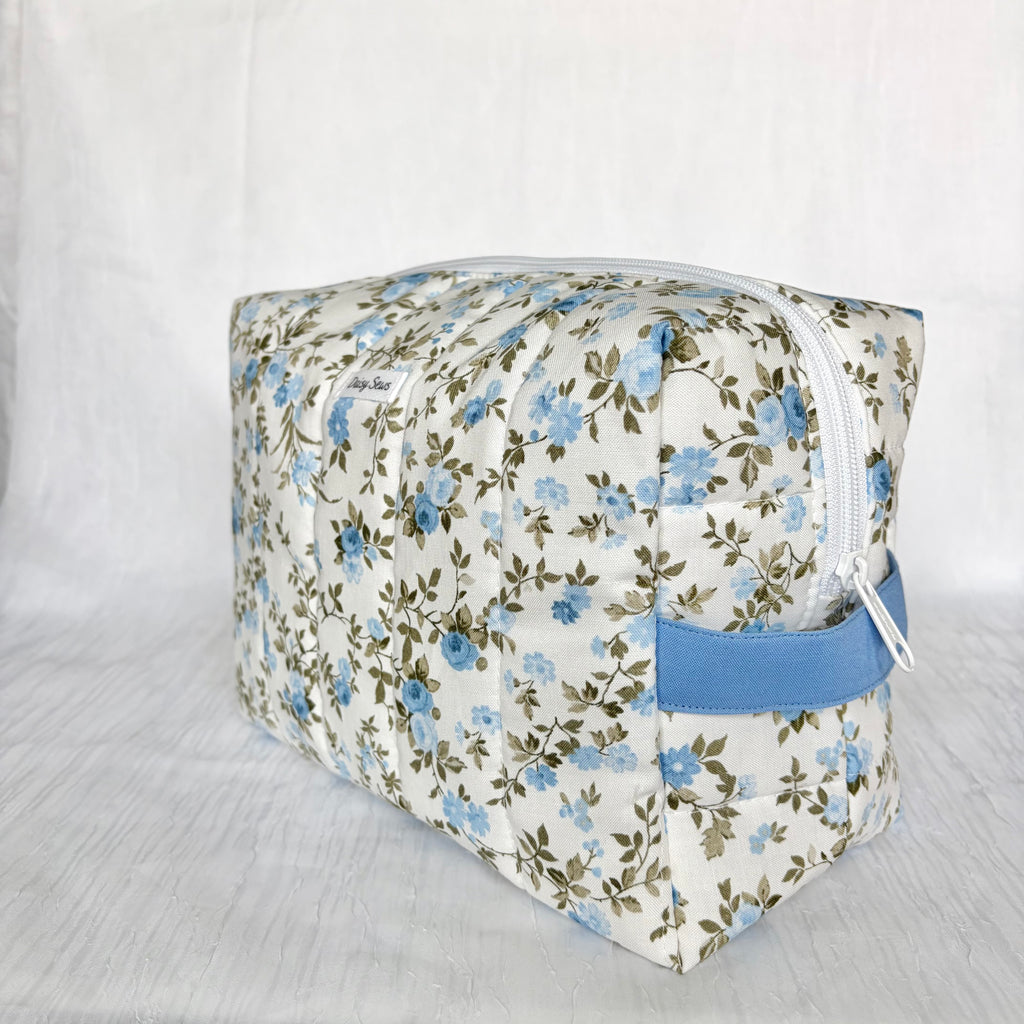 A rectangular zippered pouch with a white background and a blue floral pattern, featuring a solid blue fabric loop handle on the side.