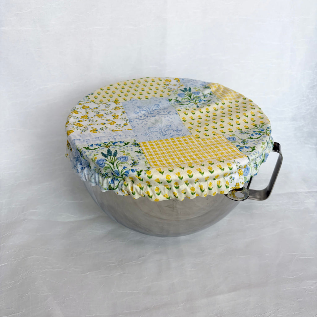 Blue and yellow floral patchwork cover on a silver metal bowl with handle on white background