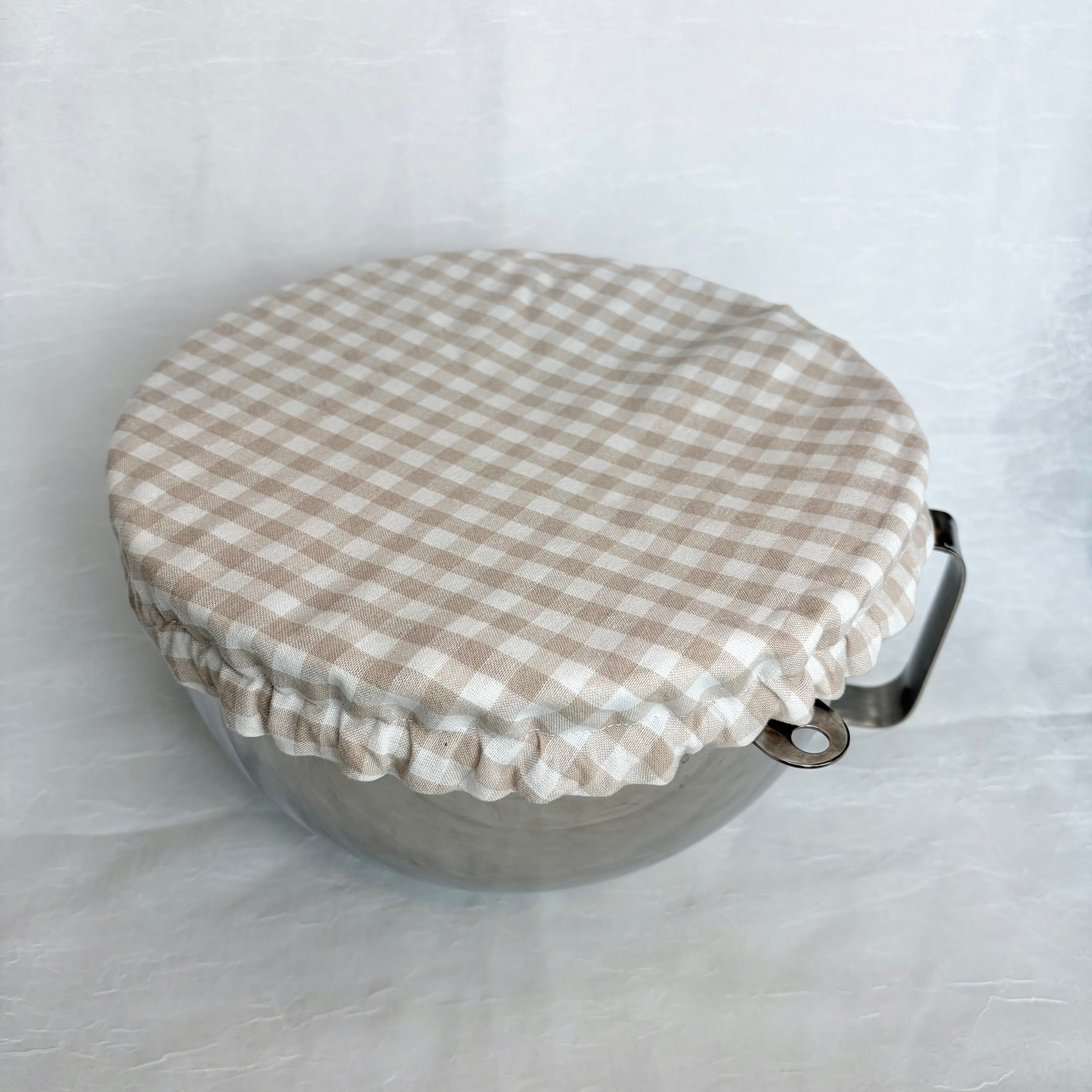 Beige gingham fabric cover on metal bowl on white background