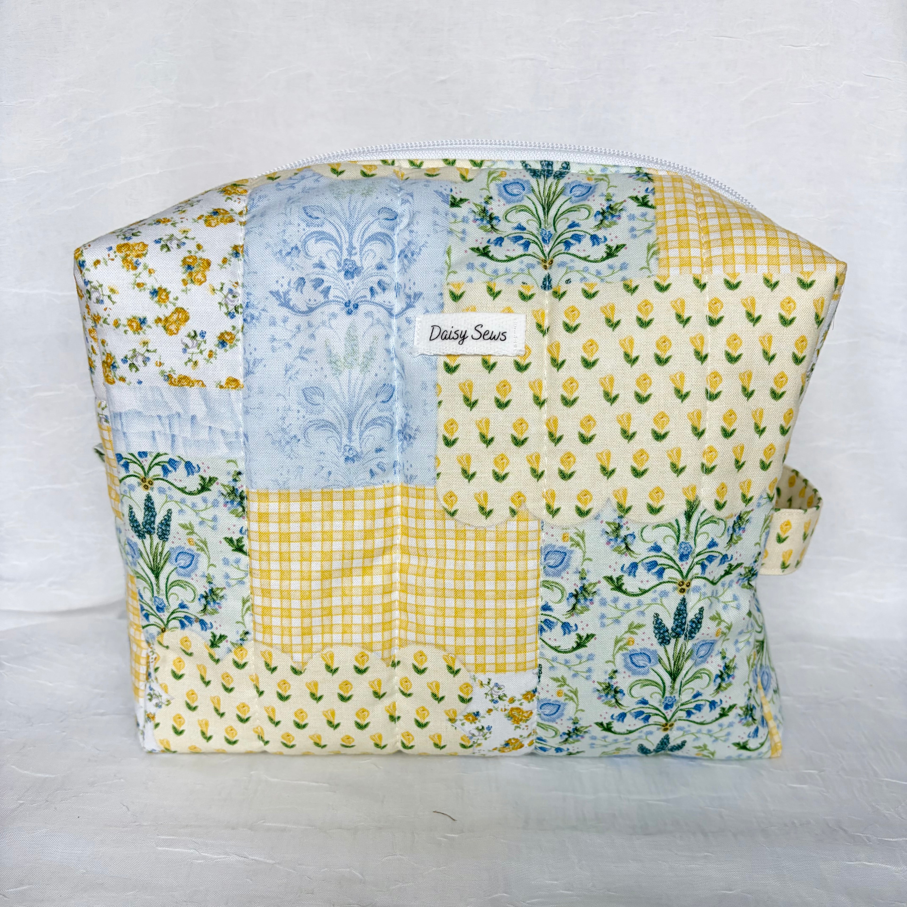  blue and yellow floral patchwork boxy bag with white label and zipper against white background