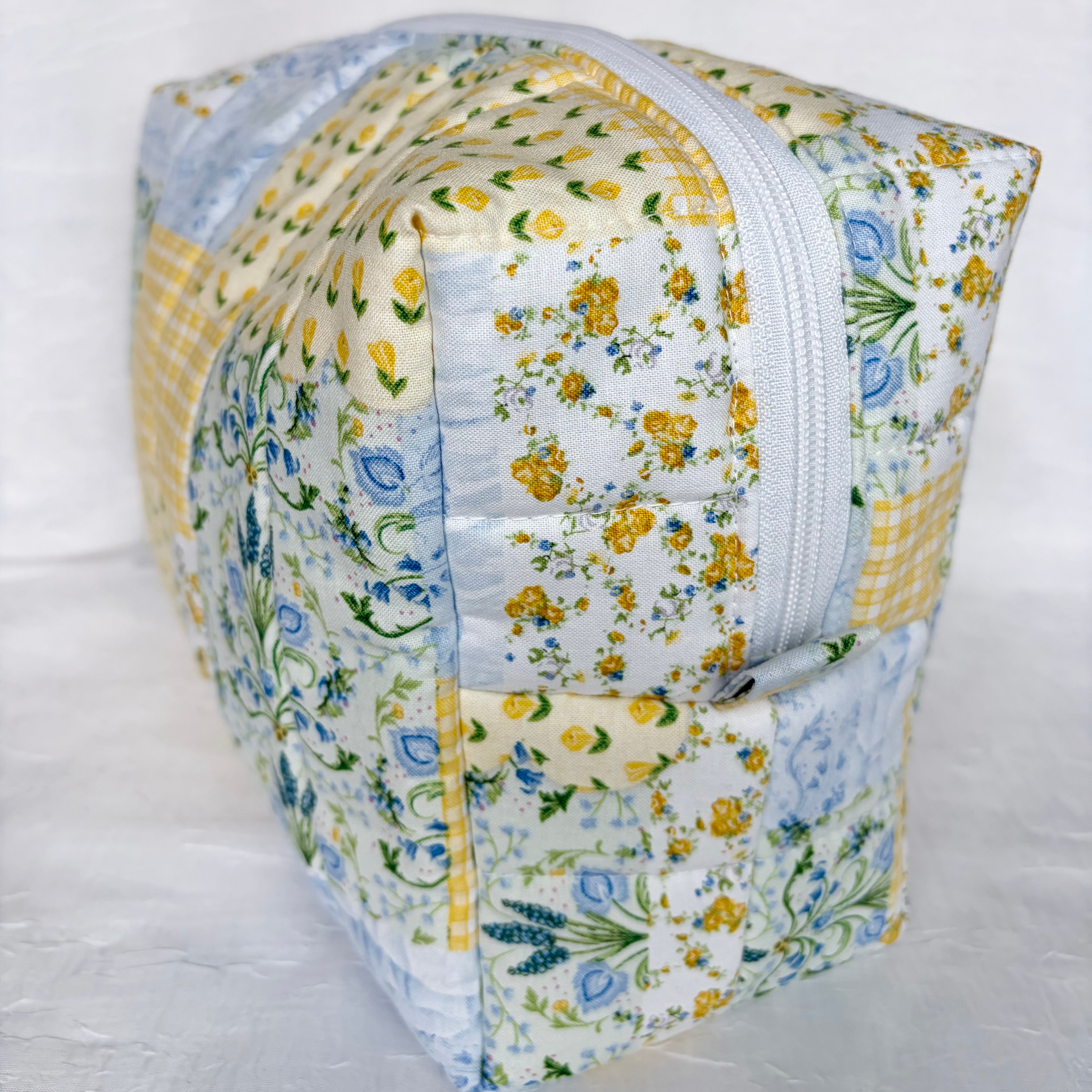 side view of pull tab and white zipper on blue and yellow floral patchwork boxy bag against white background