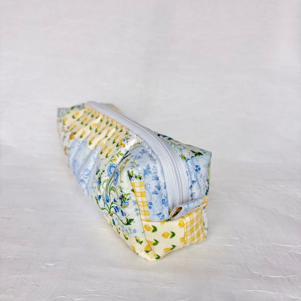 Side view of pull tab on blue and yellow floral patchwork boxy bag against white background