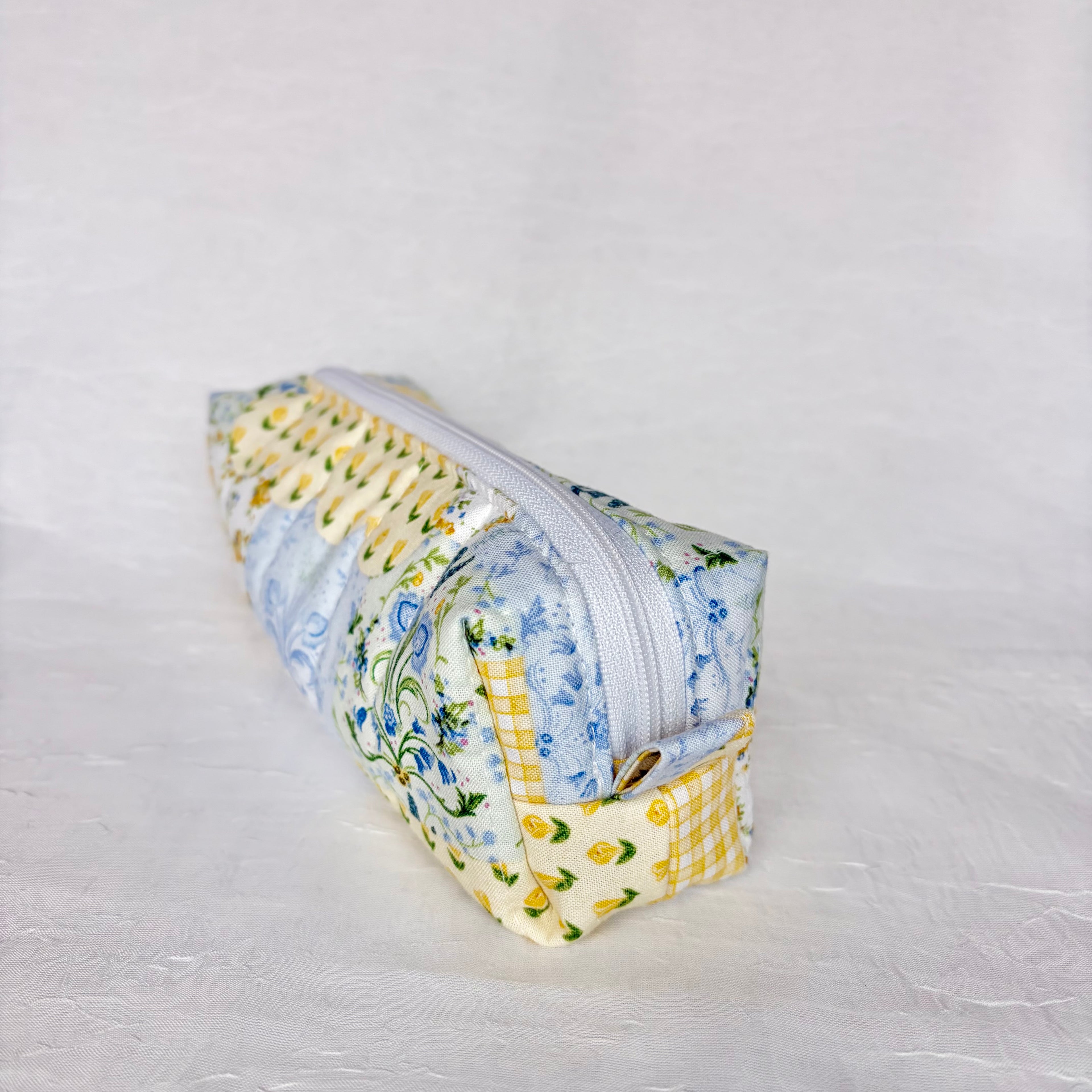 Side view of pull tab on blue and yellow floral patchwork boxy bag against white background