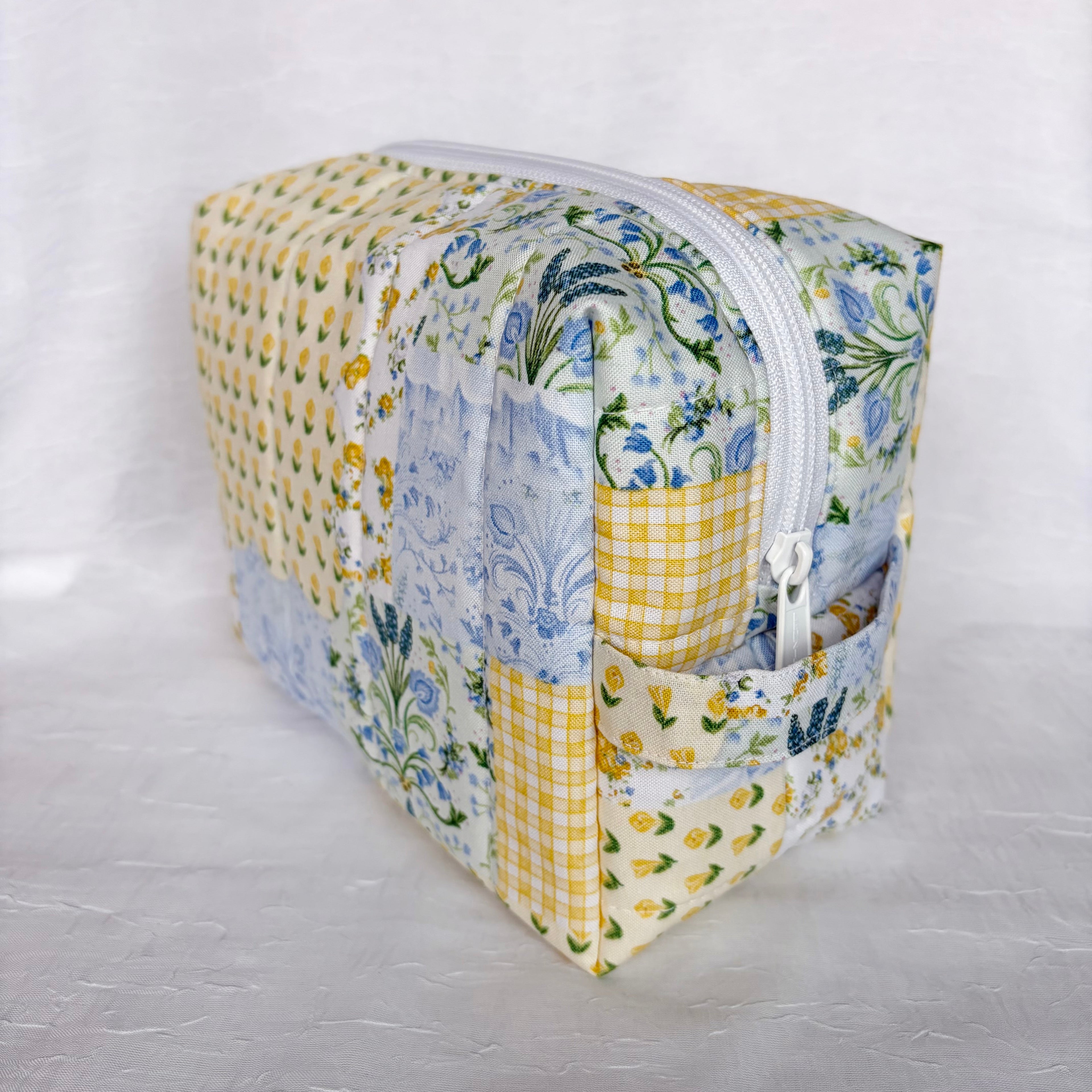 side view of handle on Blue and Yellow floral Patchwork boxy bag with white zipper against white background
