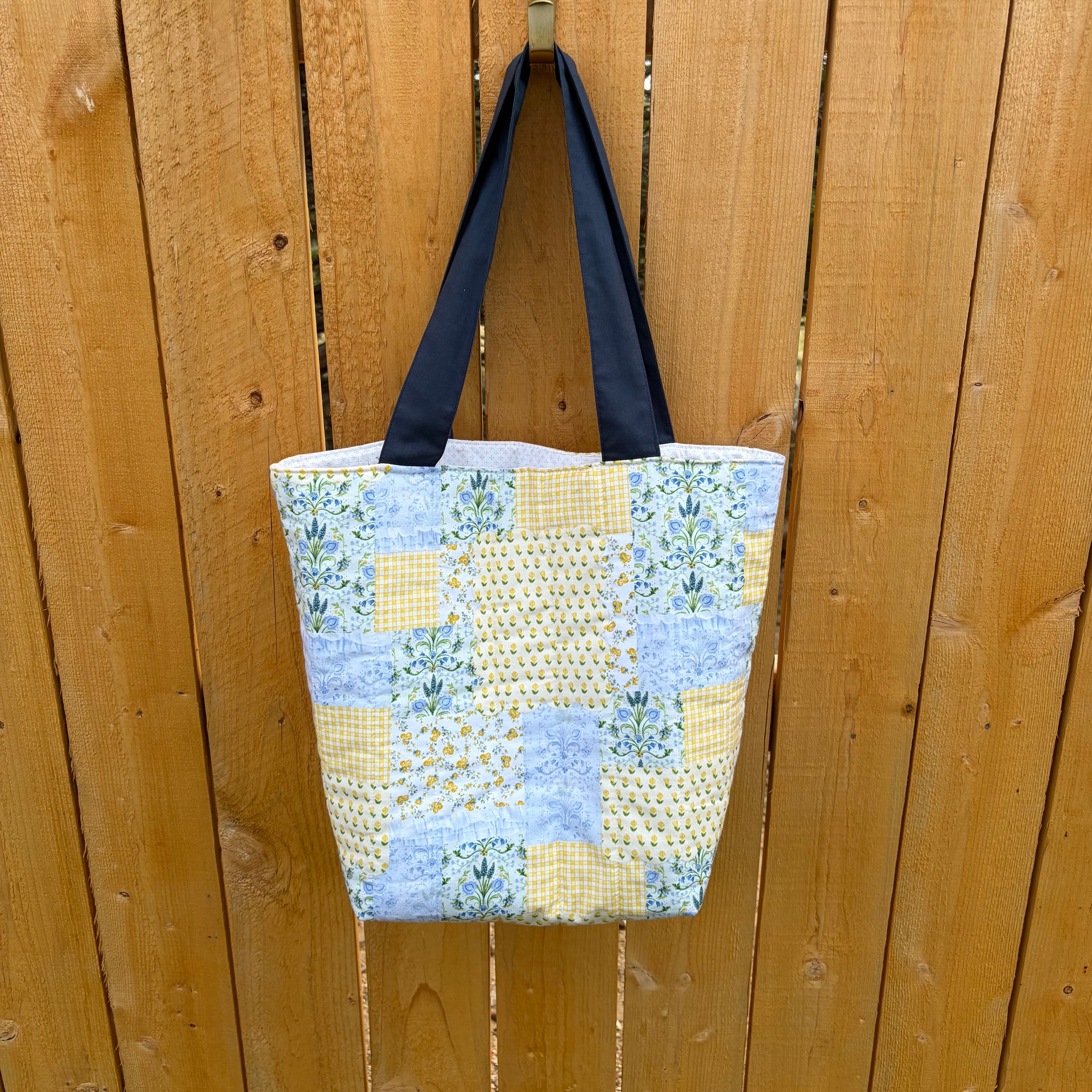 Blue and Yellow floral Patchwork Tote Bag with navy handles hanging on wooden fence