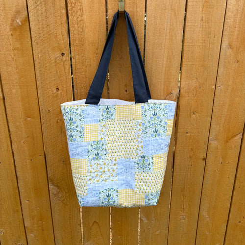 Blue and Yellow floral Patchwork Tote Bag with navy handles hanging on wooden fence