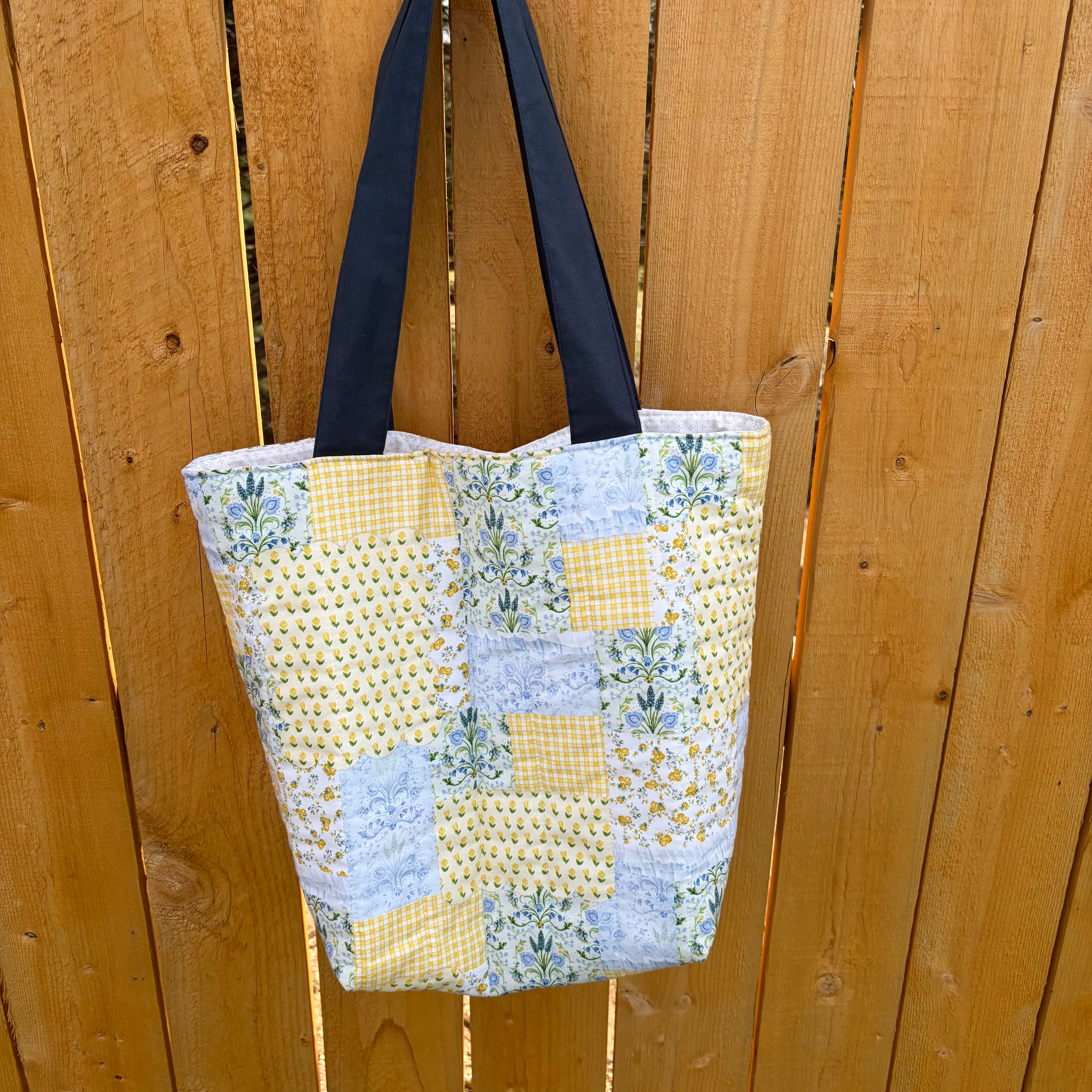 Back View of Blue and Yellow floral Patchwork Tote Bag with navy handles hanging on wooden fence