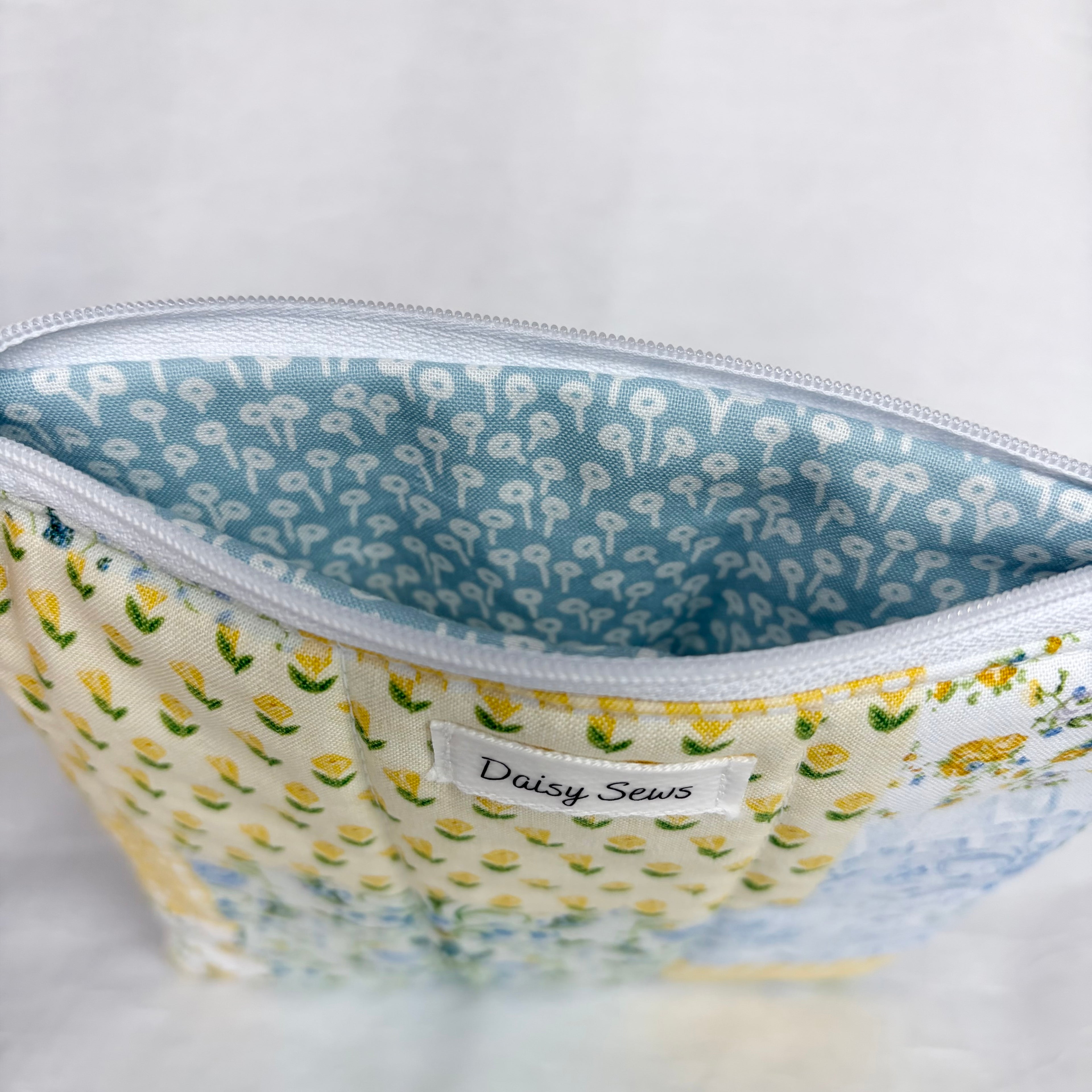 yellow and blue floral exterior with blue interior with white flower design and white zipper at top opening on white background