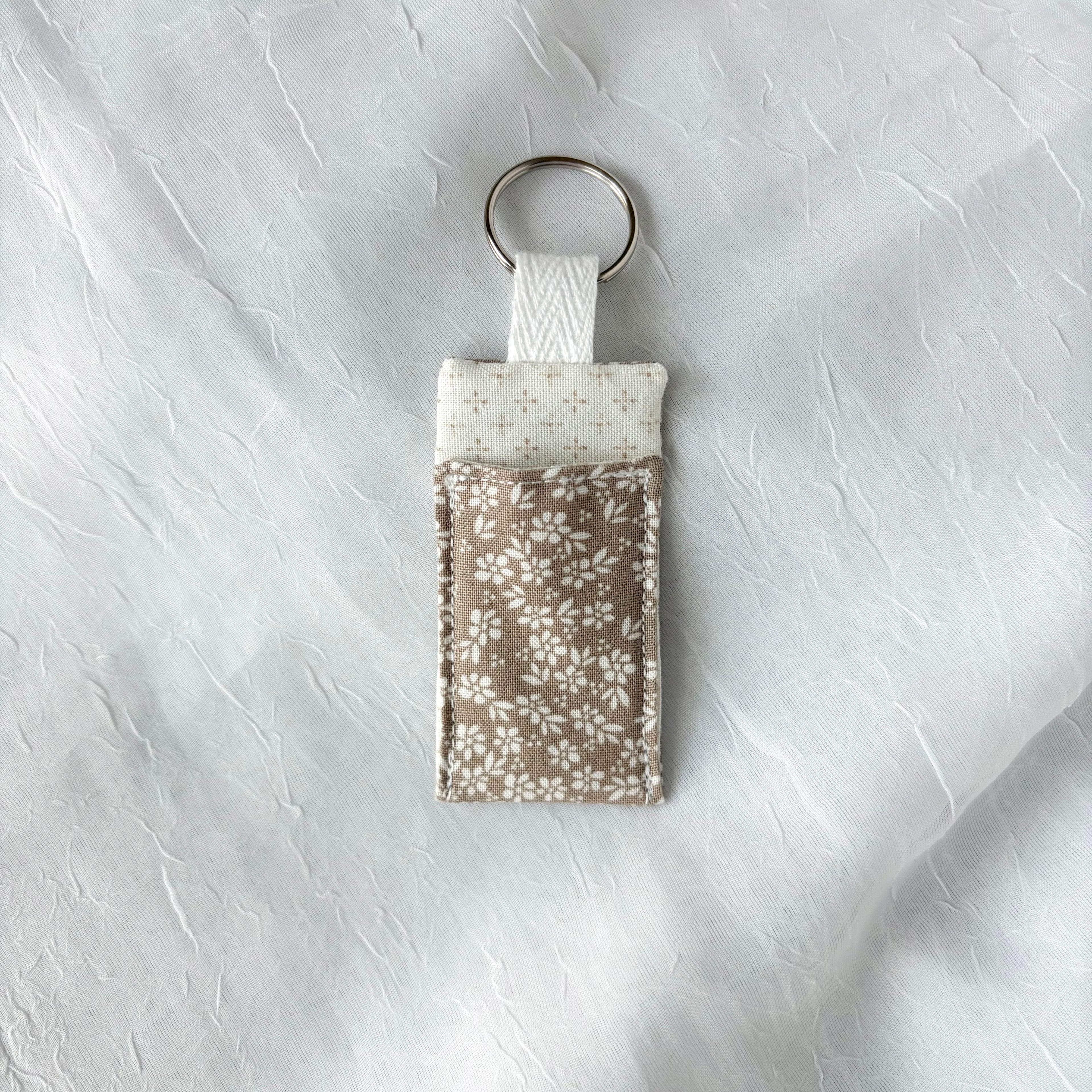 Cream Floral on brown fabric with cream dotted liner chapstick holder with keychain ring on a textured gray background