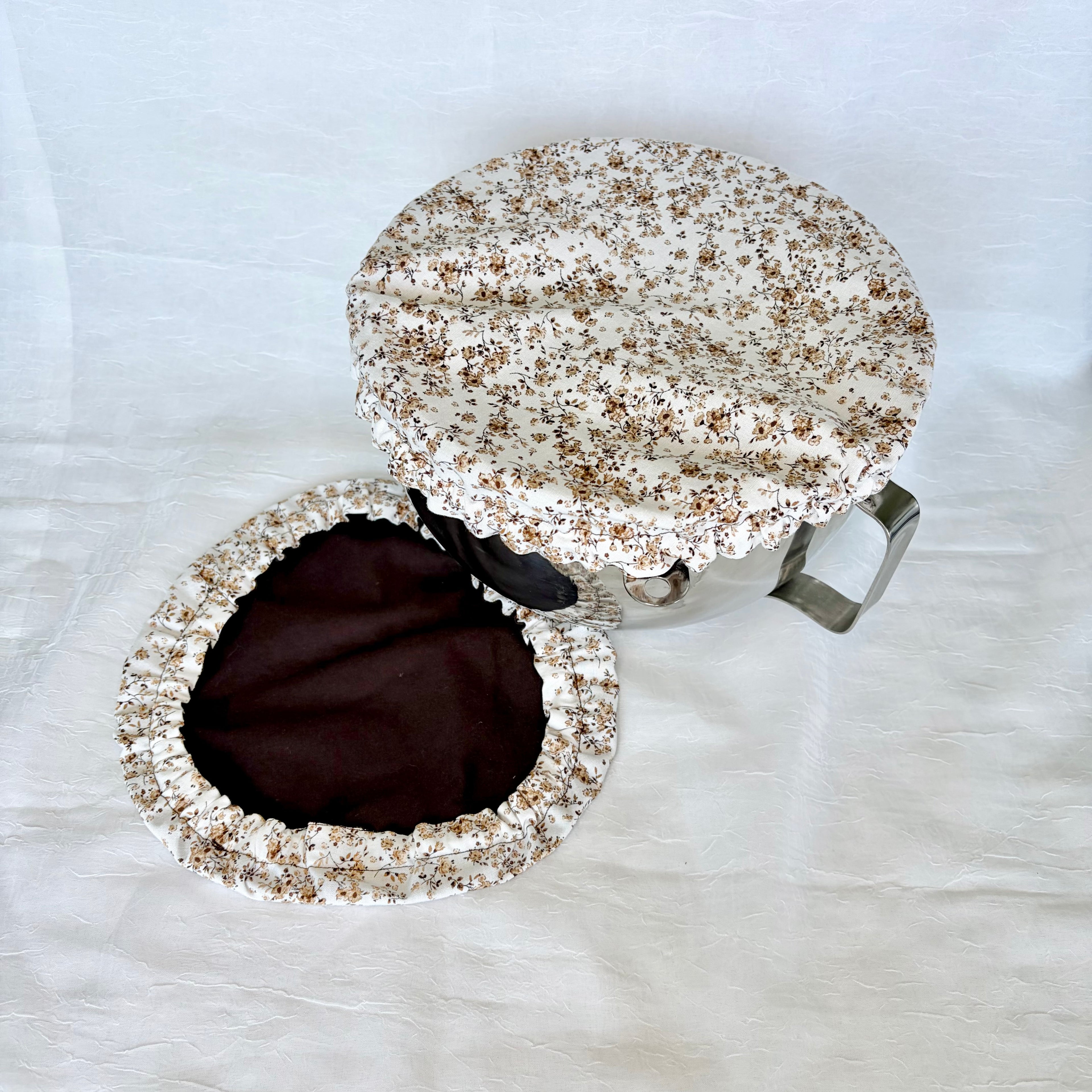 white bowl cover with tiny brown floral design on silver bowl with white background. Dark brown cover on surface.