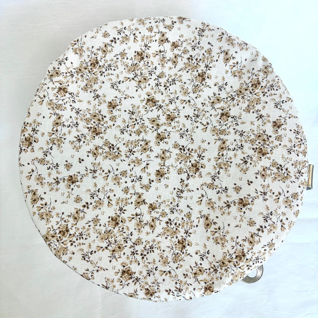 A round fabric-bowl with a dense small floral print in beige, brown, and black on an off-white background, shown from a top-down view.