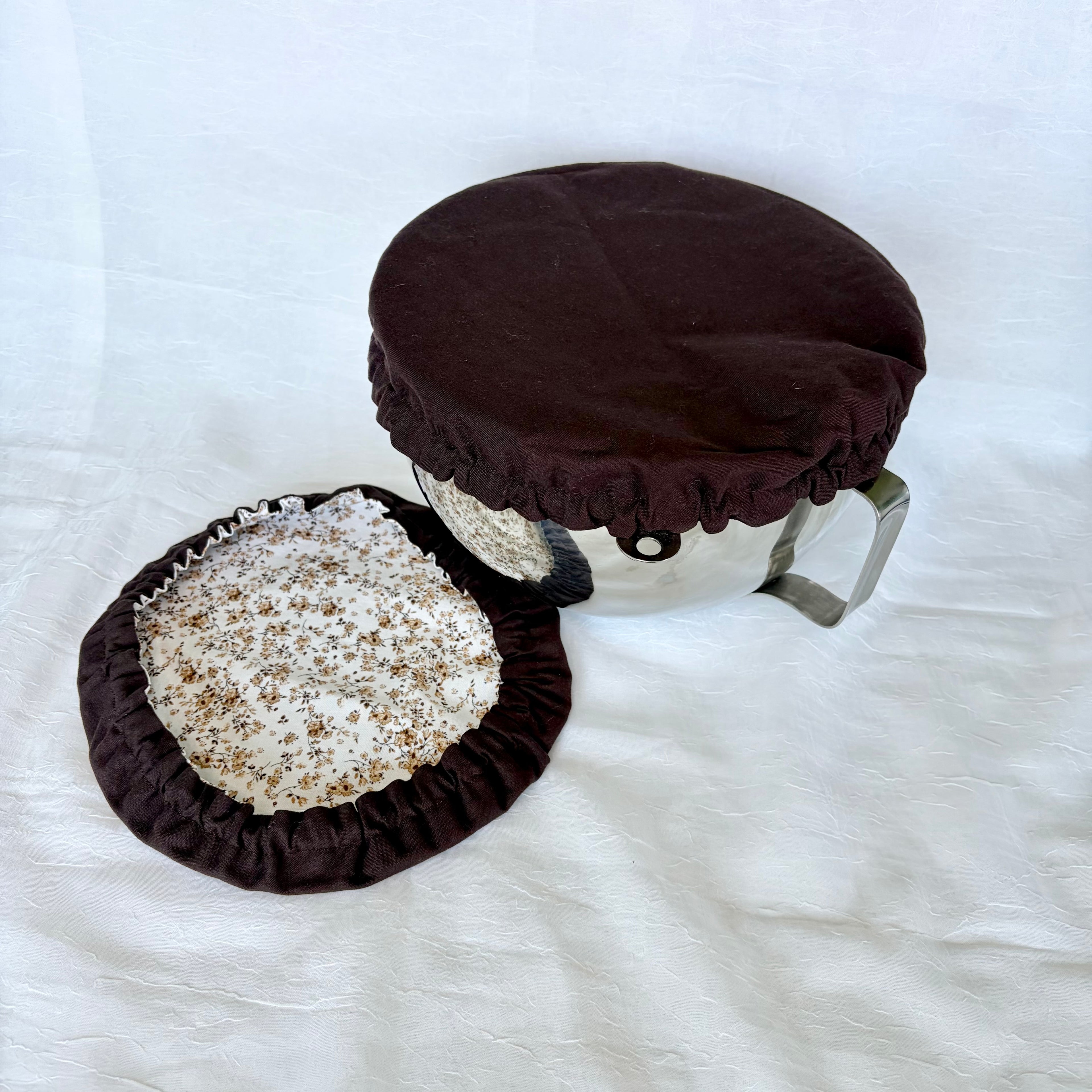 dark brown bowl cover on silver bowl with white background. brown cover with brown floral design on surface.