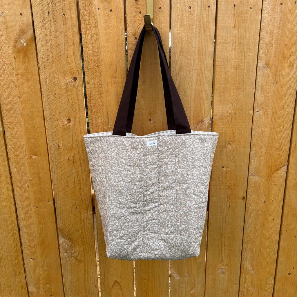 Brown floral tote bag with dark brown handles hanging on a wooden fence