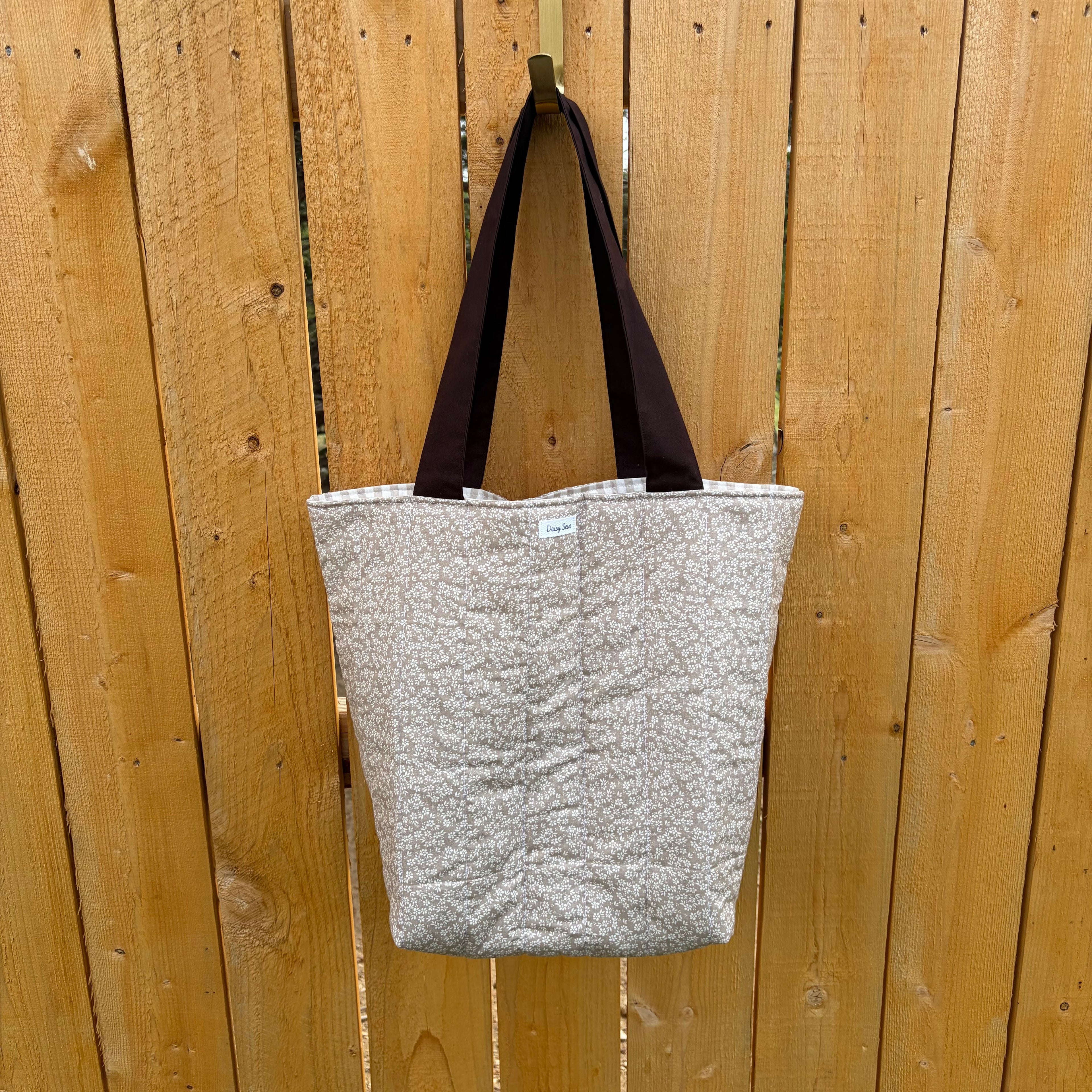 Brown floral tote bag with dark brown handles hanging on a wooden fence