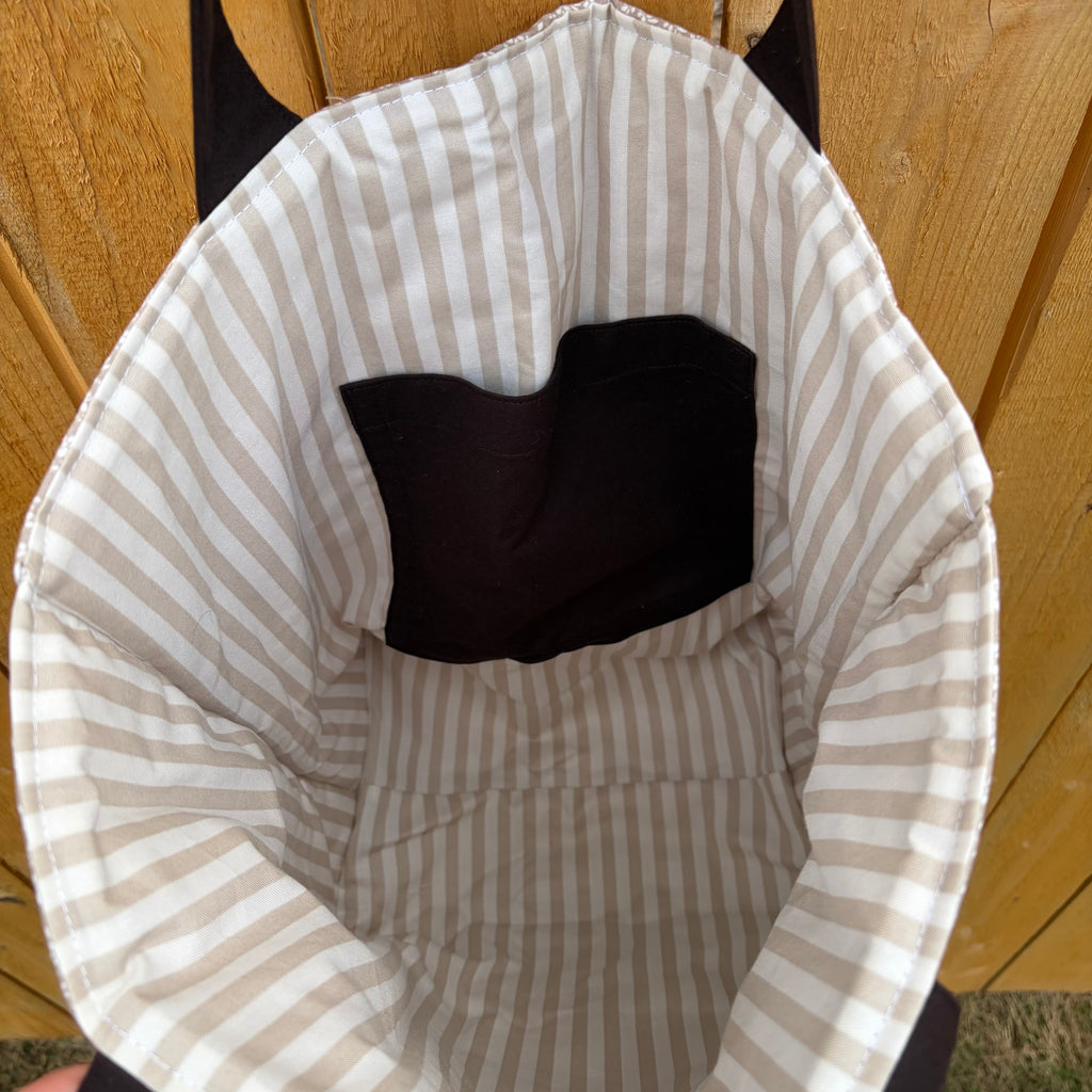 tan and white vertical striped liner  with dark brown pocket and matching handles hanging on a wooden fence