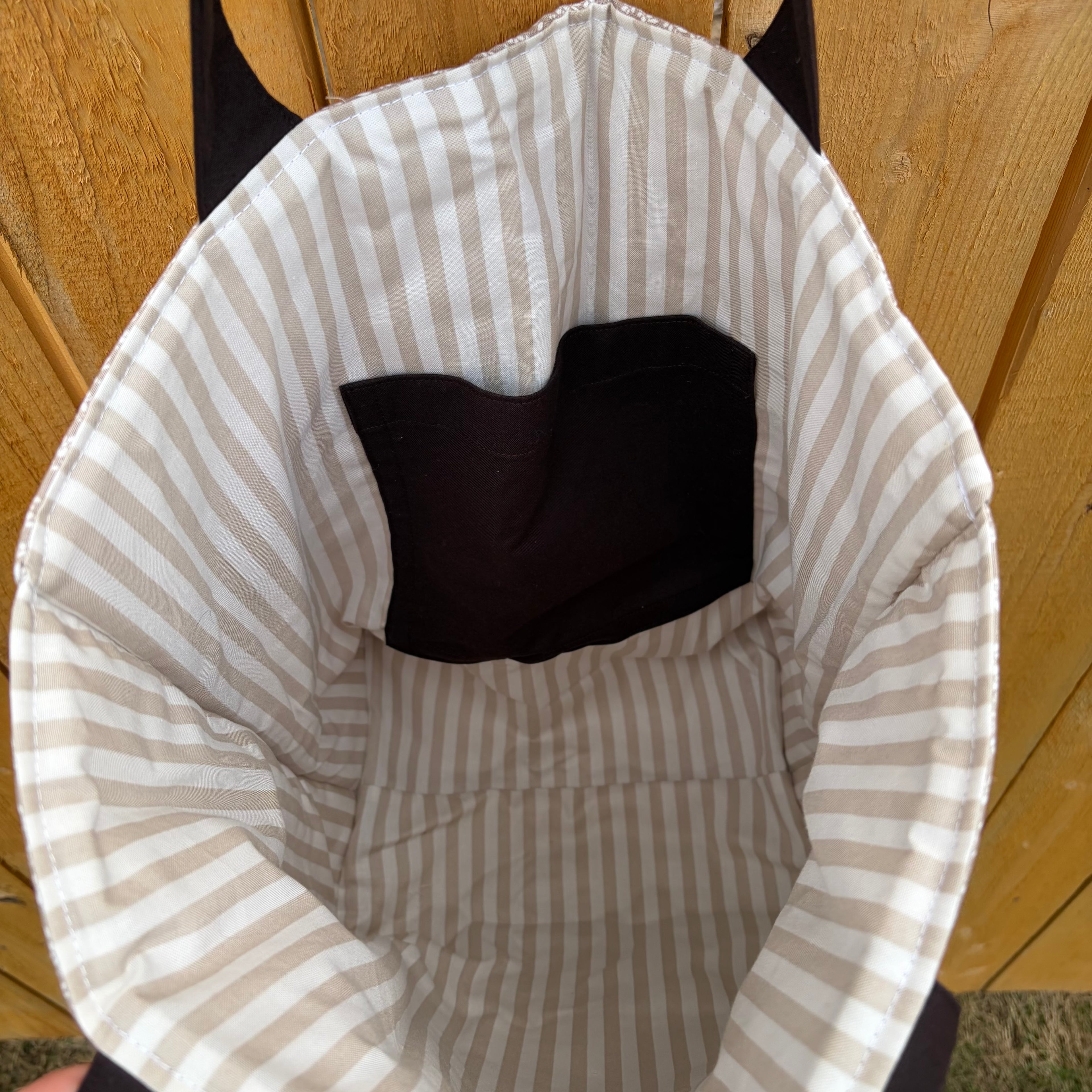 tan and white vertical striped liner  with dark brown pocket and matching handles hanging on a wooden fence