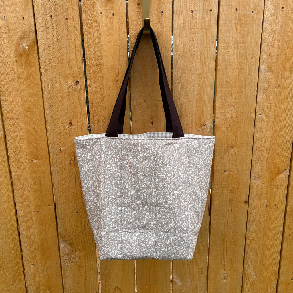 back view Brown floral tote bag with dark brown handles hanging on a wooden fence