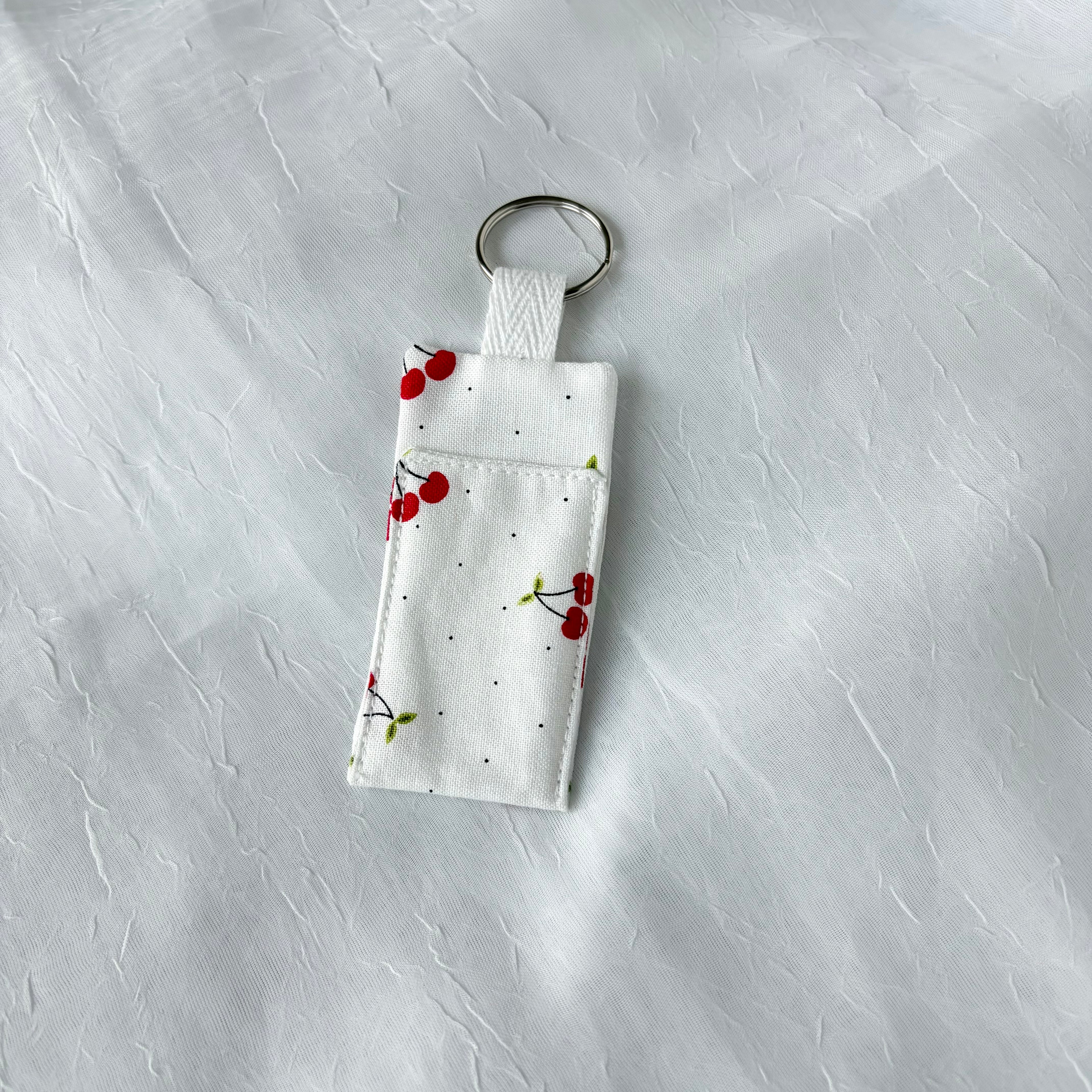 Cherry on white fabric with tiny black dots chapstick holder with keychain ring on a textured white background